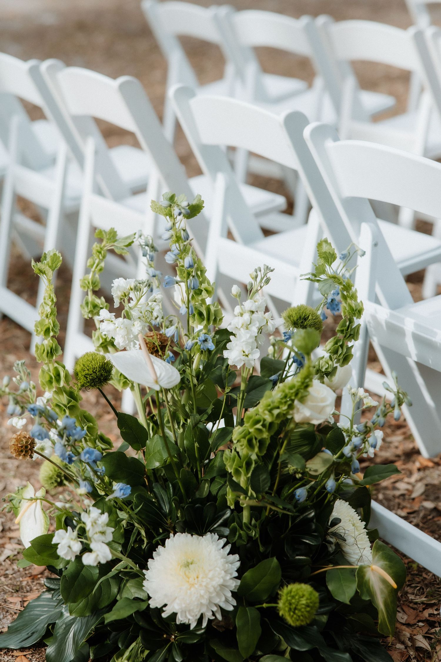 Elegant white and blue floral arrangement with delphinium and chrysanthemums decorating wedding ceremony chairs.