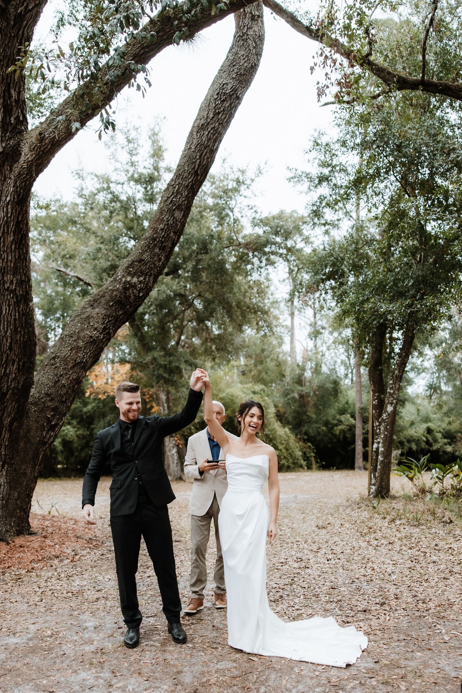 A couple celebrates joyfully on a tree-lined path during their wedding celebration.