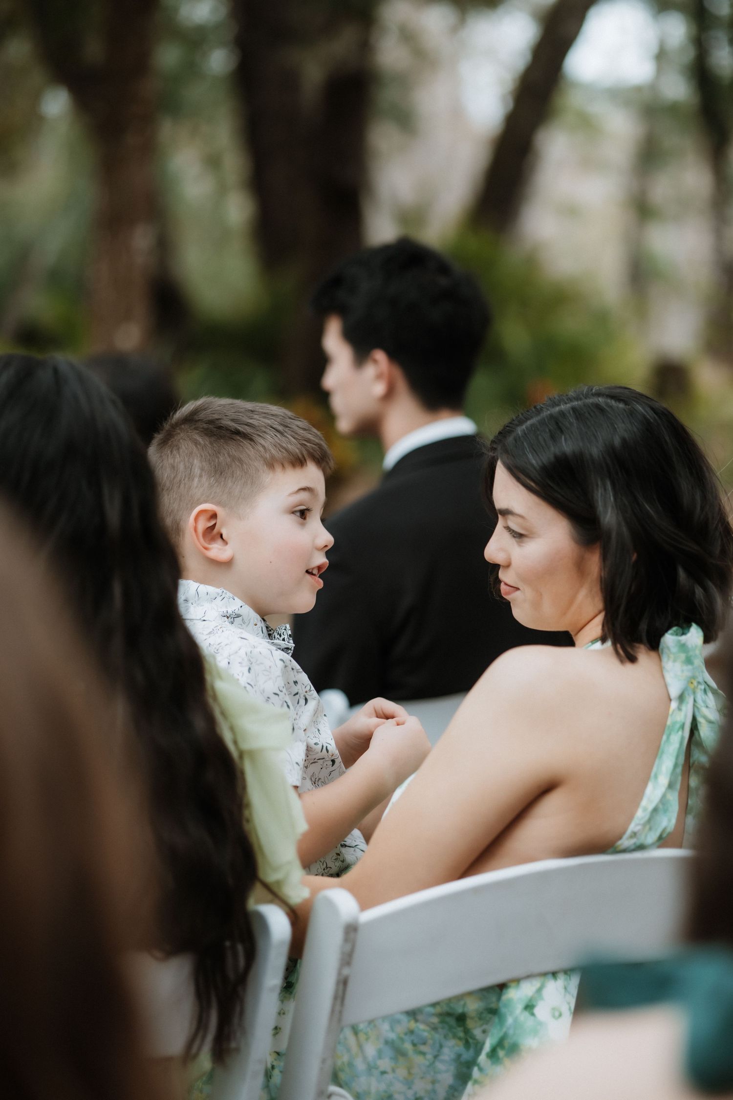 Intimate conversation during outdoor wedding ceremony seating under oak trees.
