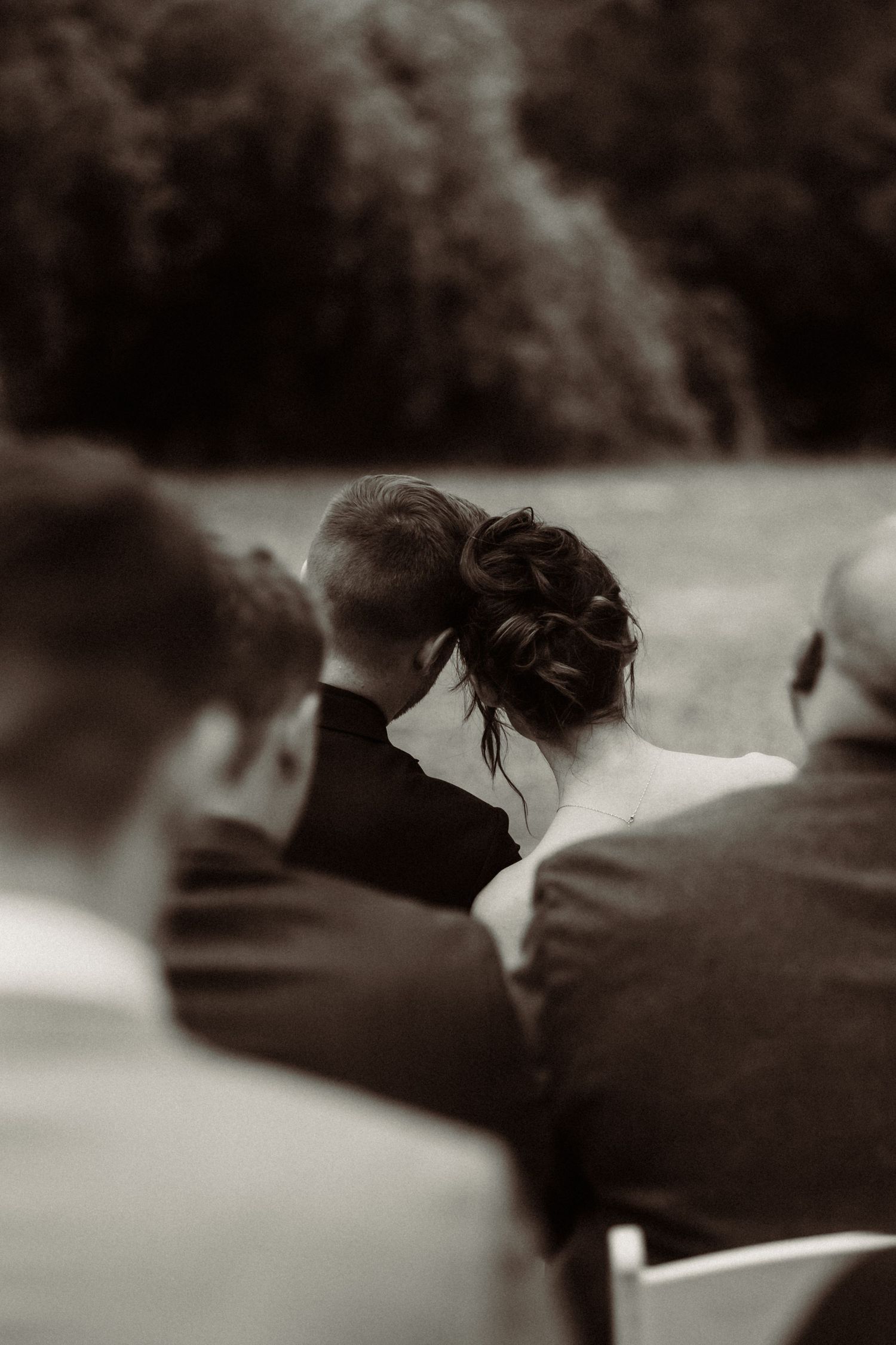 A black and white photo captures guests seated at an outdoor wedding ceremony.