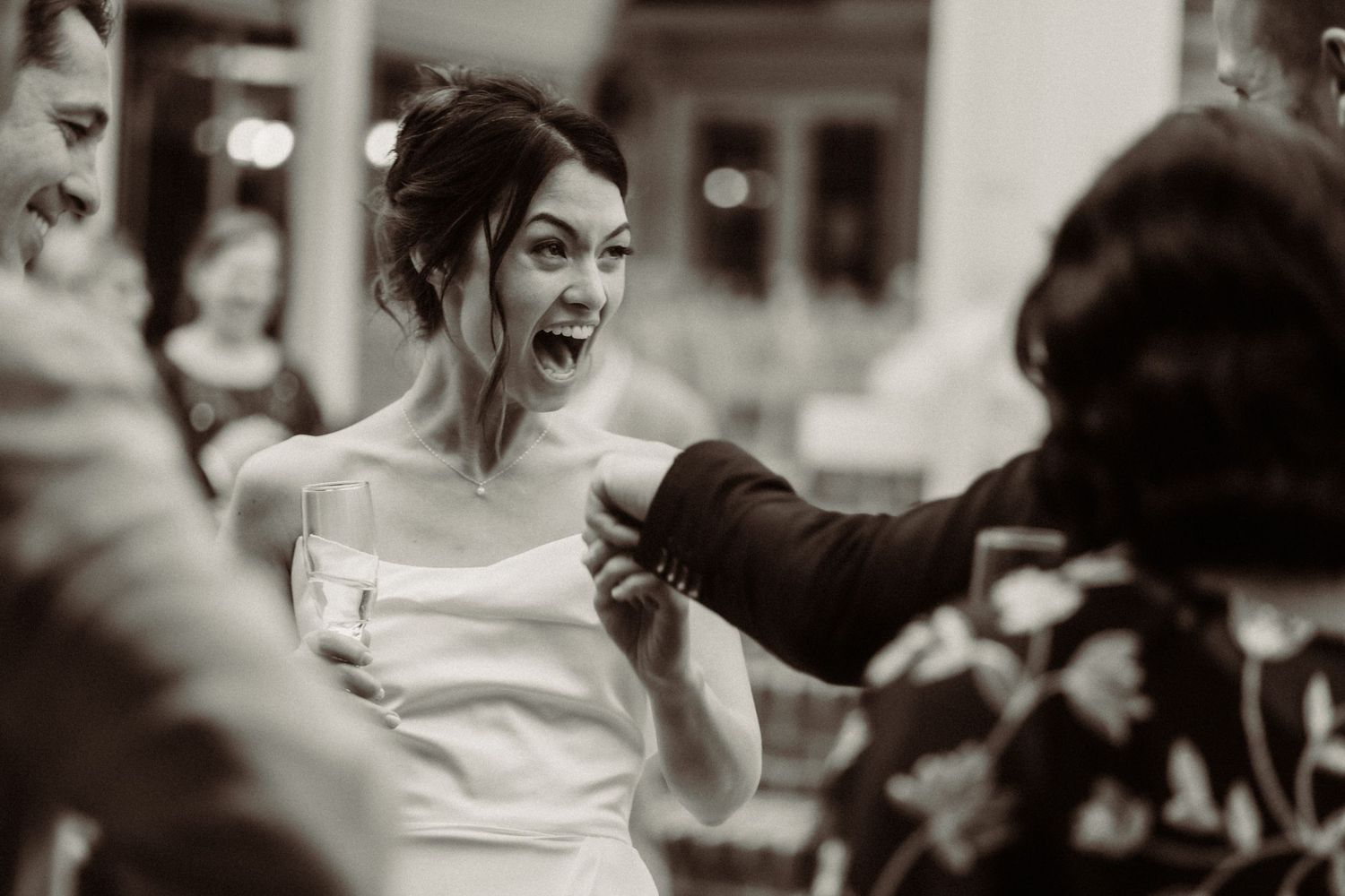 A candid black and white photo captures a joyful reaction during a wedding reception.