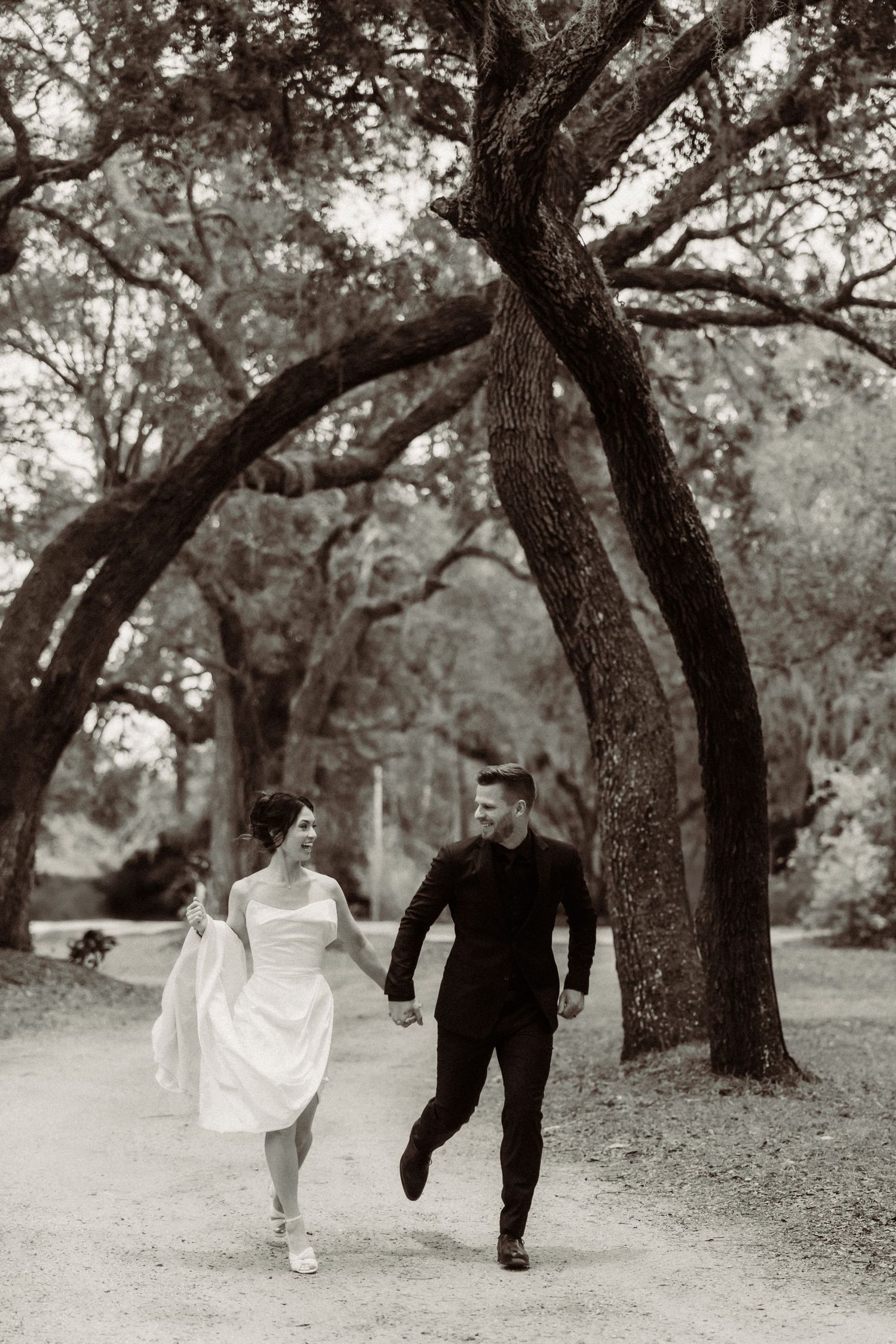 Black and white photo of a couple running playfully along a tree-lined path.