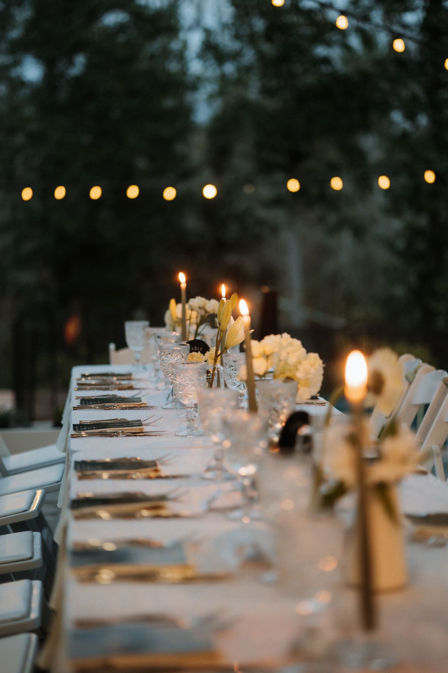 An elegant wedding reception table setting with twinkling lights and white decor in the evening.