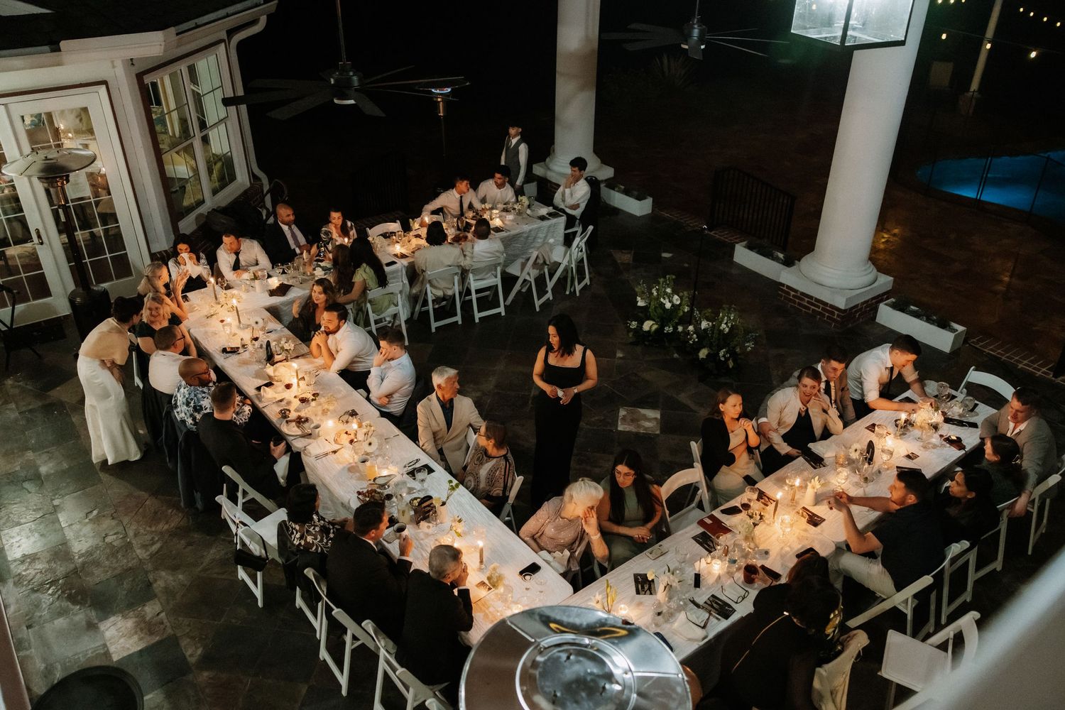 Wedding reception dinner setup with U-shaped table arrangement illuminated by warm candlelight.