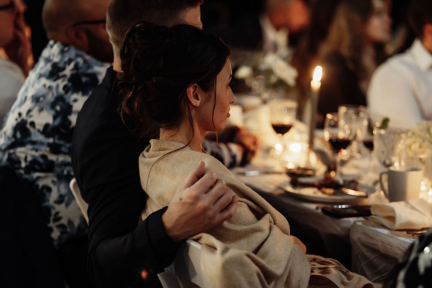 Intimate candlelit moment between guests at an evening wedding reception dinner.