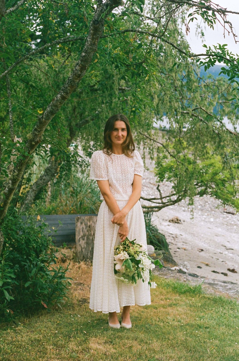 White dress against natural green backdrop with delicate floral bouquet.
