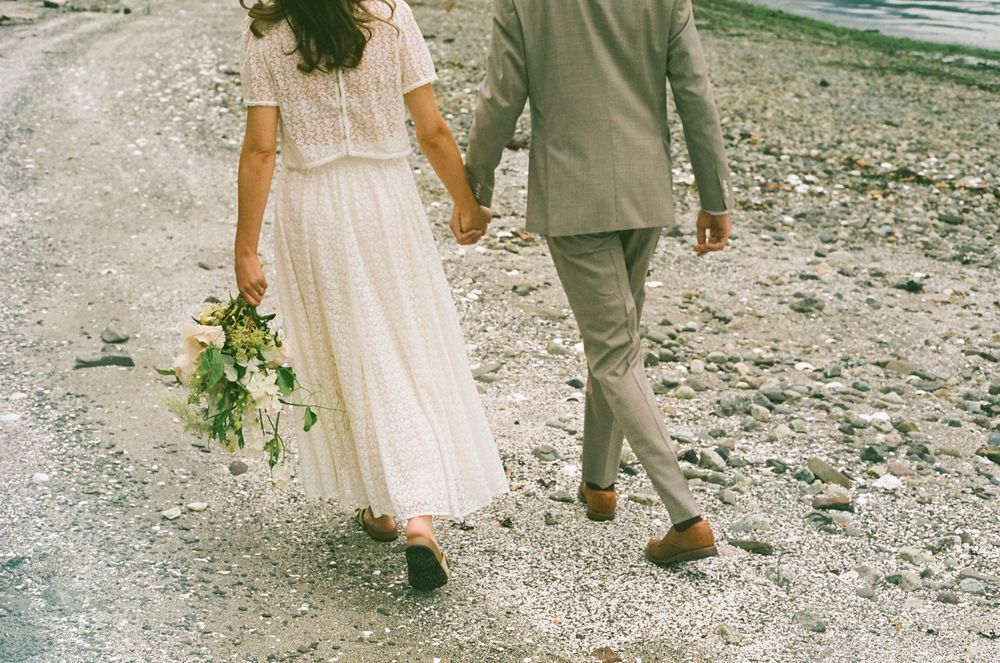 A couple walks away on a rocky path, showing detailed view of wedding attire and bouquet.