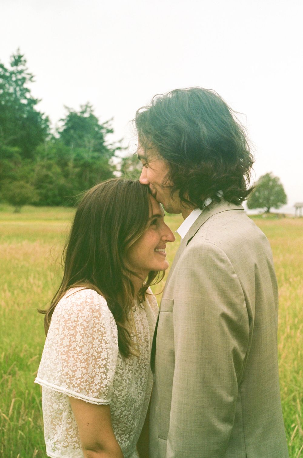 An intimate moment captured in a sunlit meadow with soft, vintage-style photography.