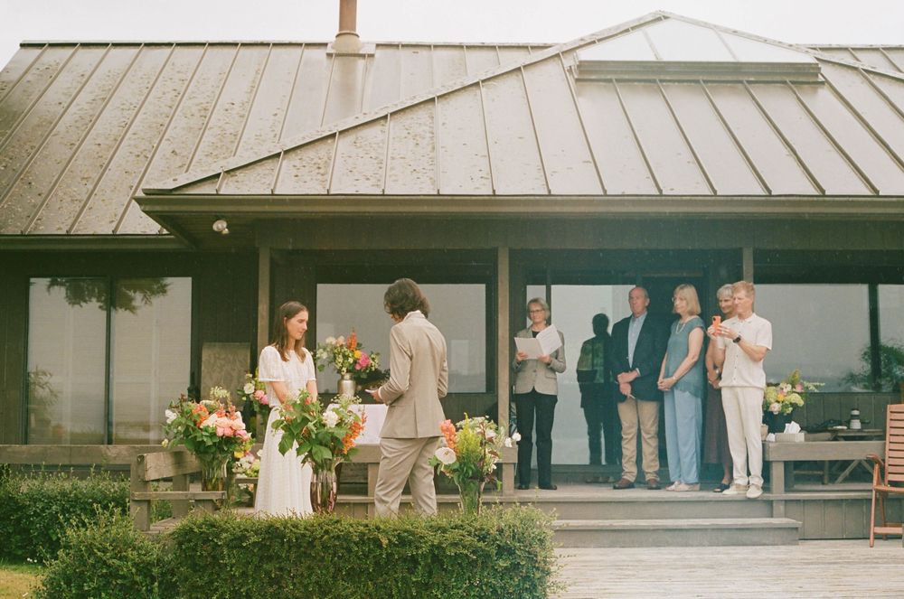 Guests gather on a covered porch of a building with white siding and metal roof.