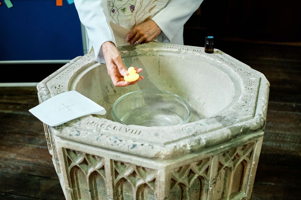 A historic stone baptismal font with Gothic architectural details being prepared for a religious ceremony.