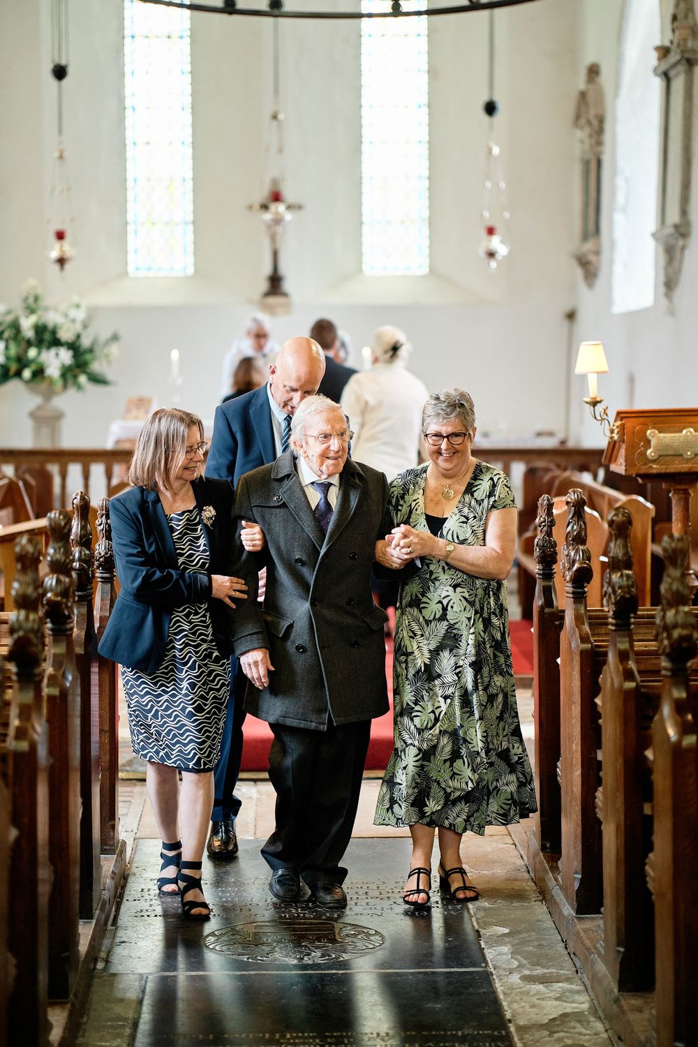 Wedding guests and family members dance joyfully down the aisle of a bright, traditional church during a celebration.