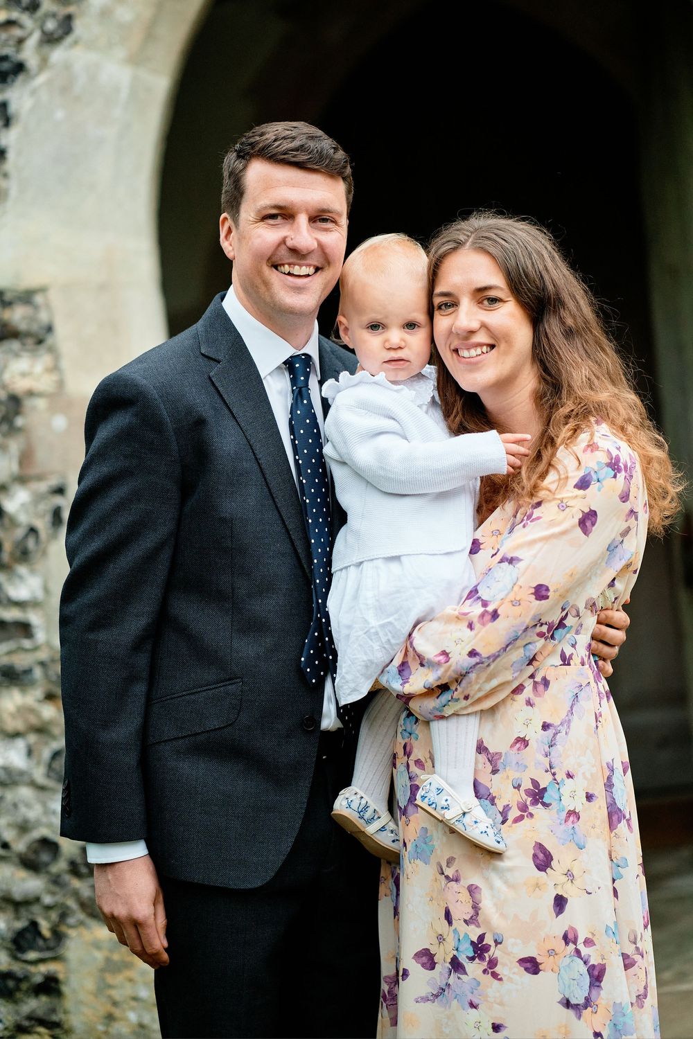 A family poses together outdoors in formal attire with a stone wall in the background.