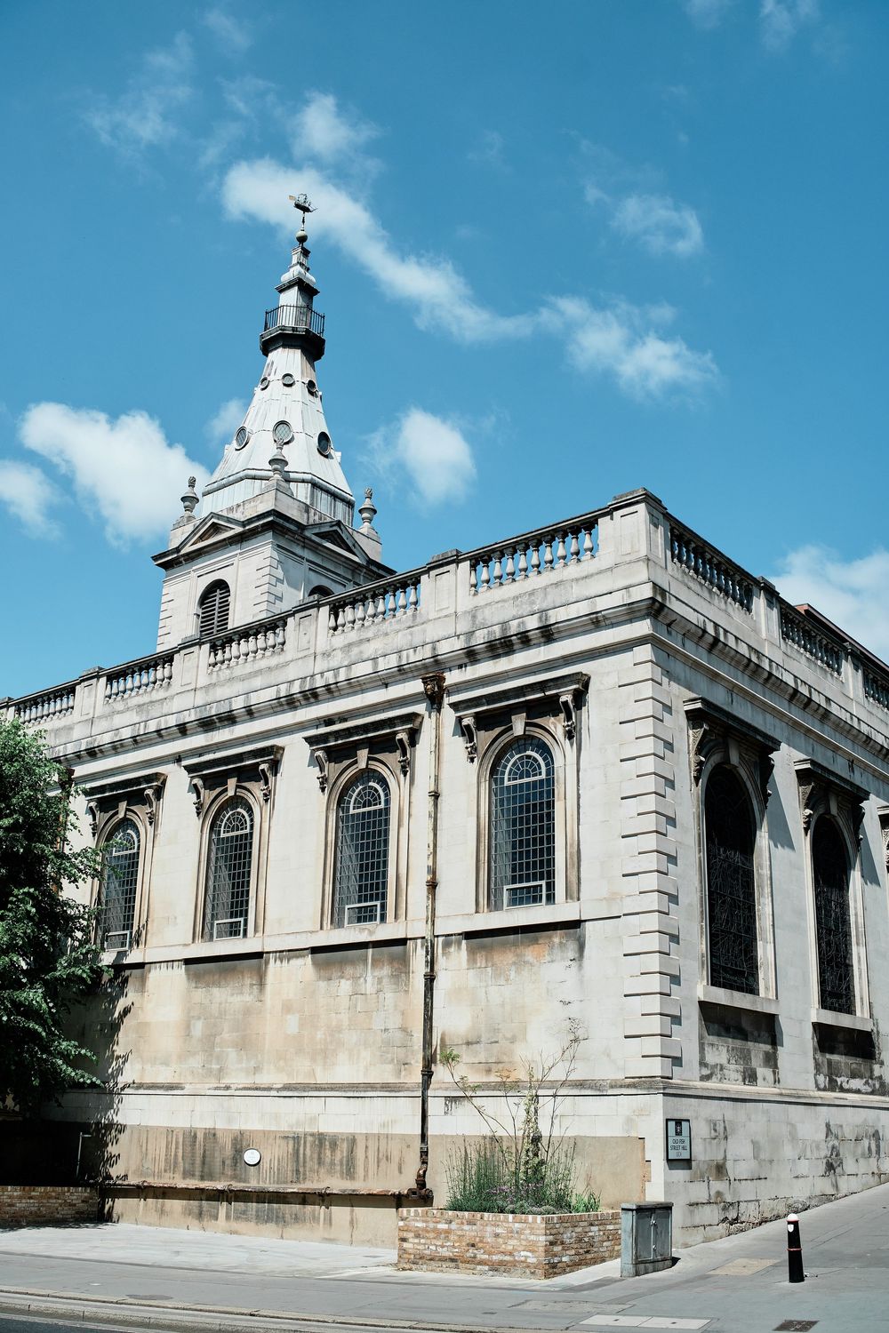 Historic white stone church building with a tall spire and arched windows against a bright blue sky.