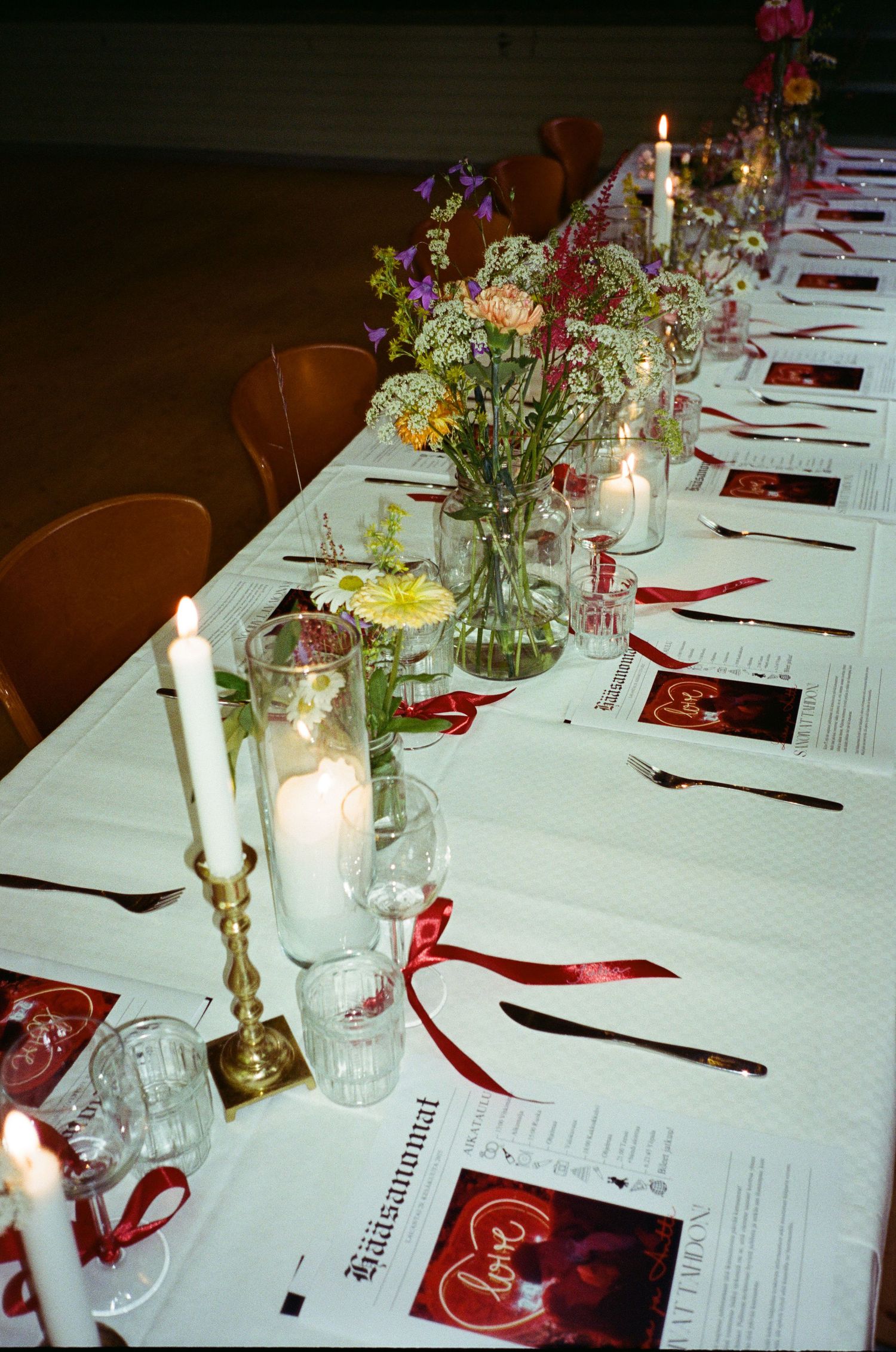 An elegant table setting for a dinner party with white tablecloth, red napkins, menus and candlesticks with fresh flowers.