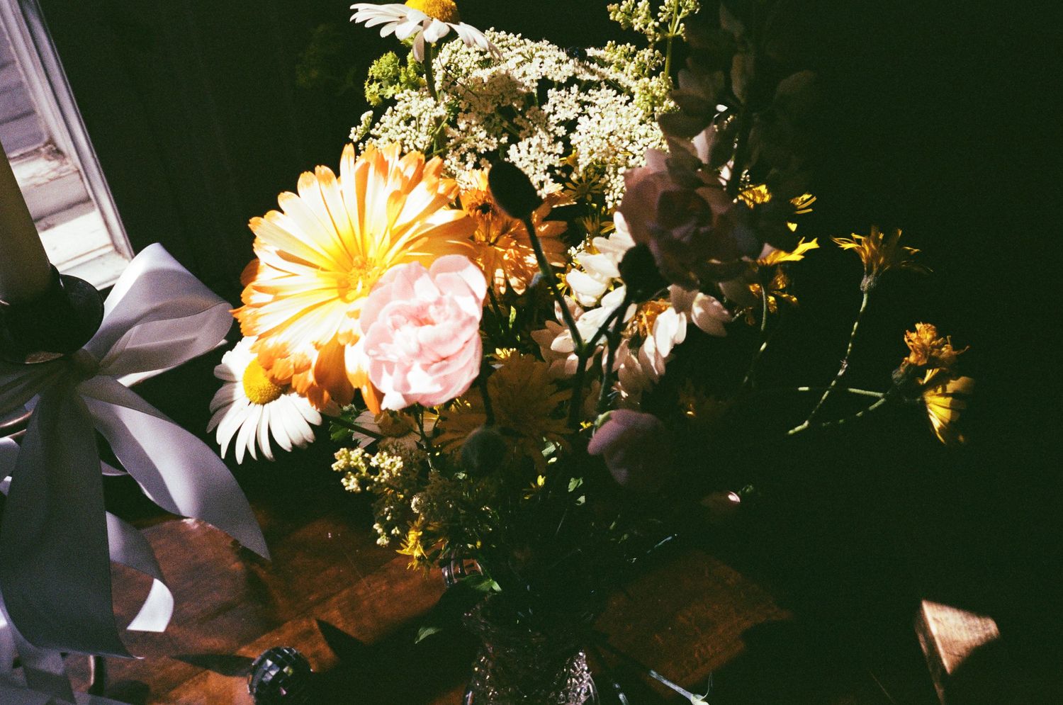 A vibrant arrangement of yellow daisies and delicate white flowers in soft sunlit lighting with film grain texture.