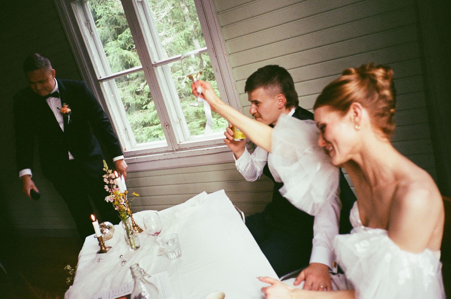 A couple in formal wedding attire react with excitement during a celebration at an indoor venue.