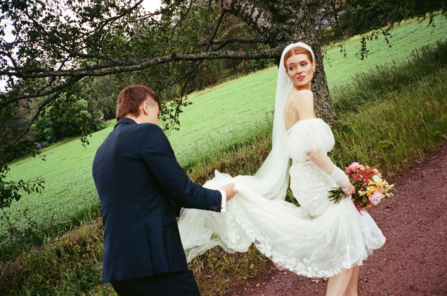 Two people sharing a romantic moment on a path with green hillside in the background.