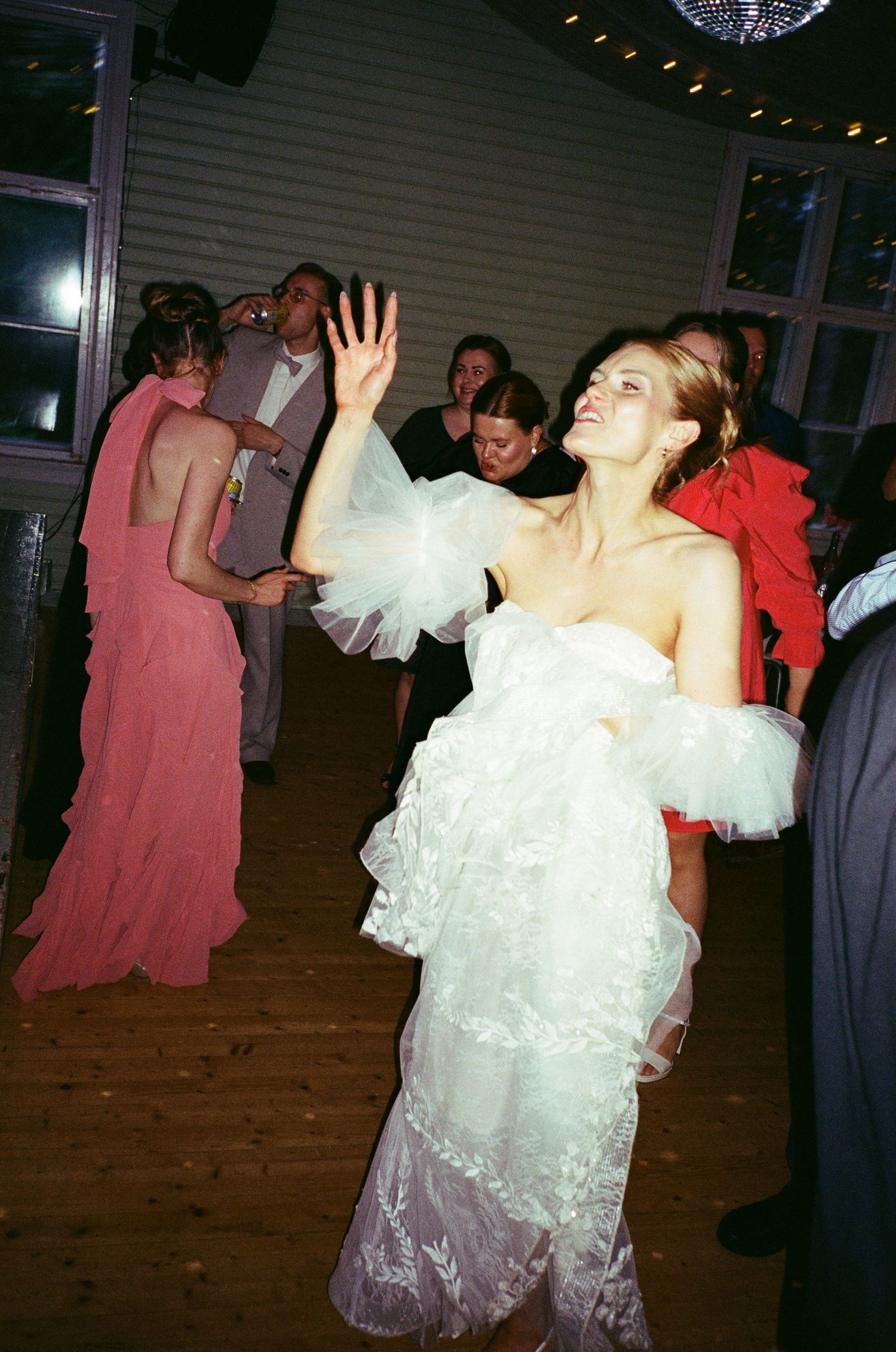 Dancing guests celebrating on the dance floor at a wedding reception with people in coral dresses and white gowns.