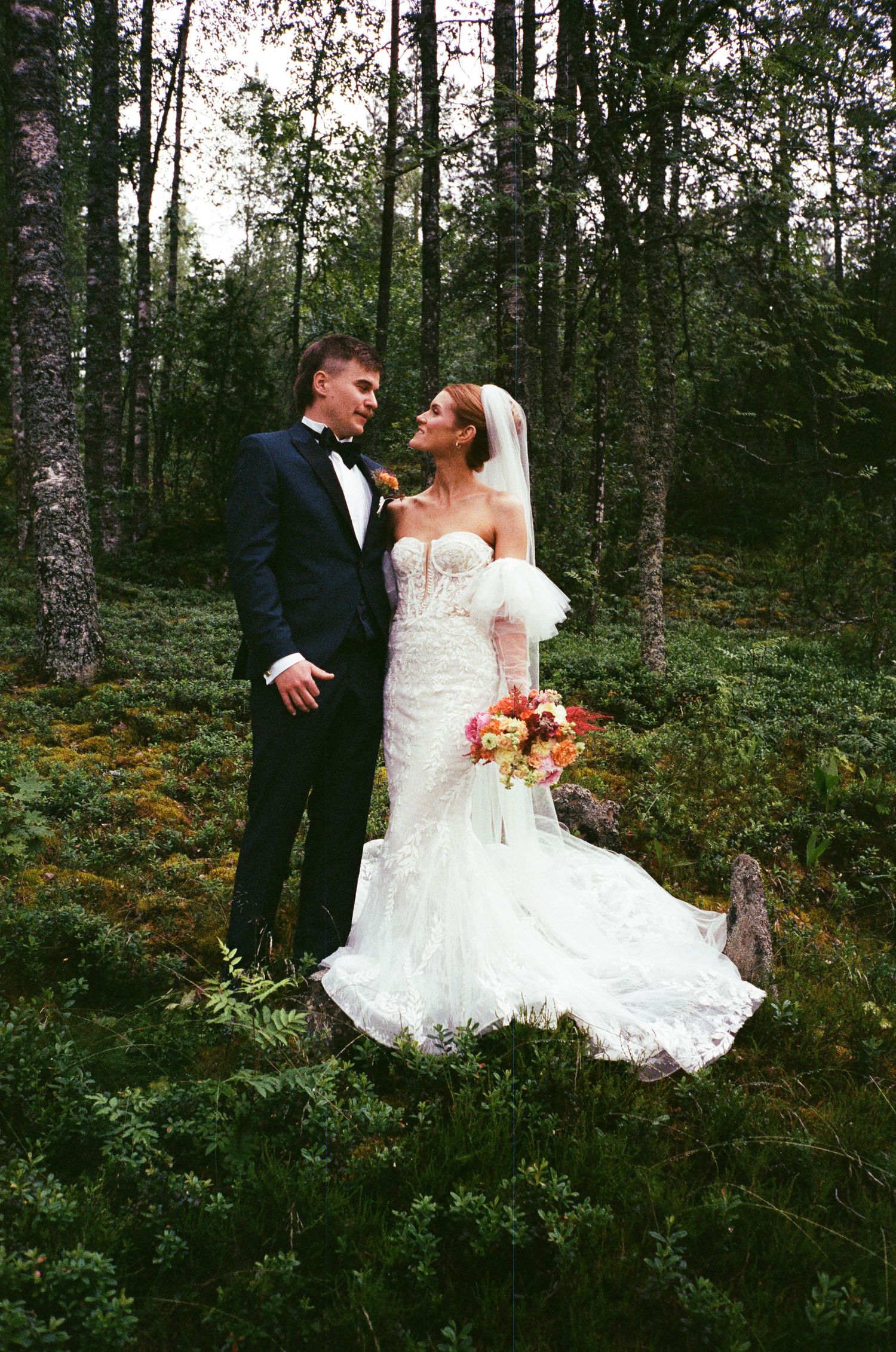 A bride and groom share romantic moments in a lush forest setting with beautiful fall foliage and natural light.