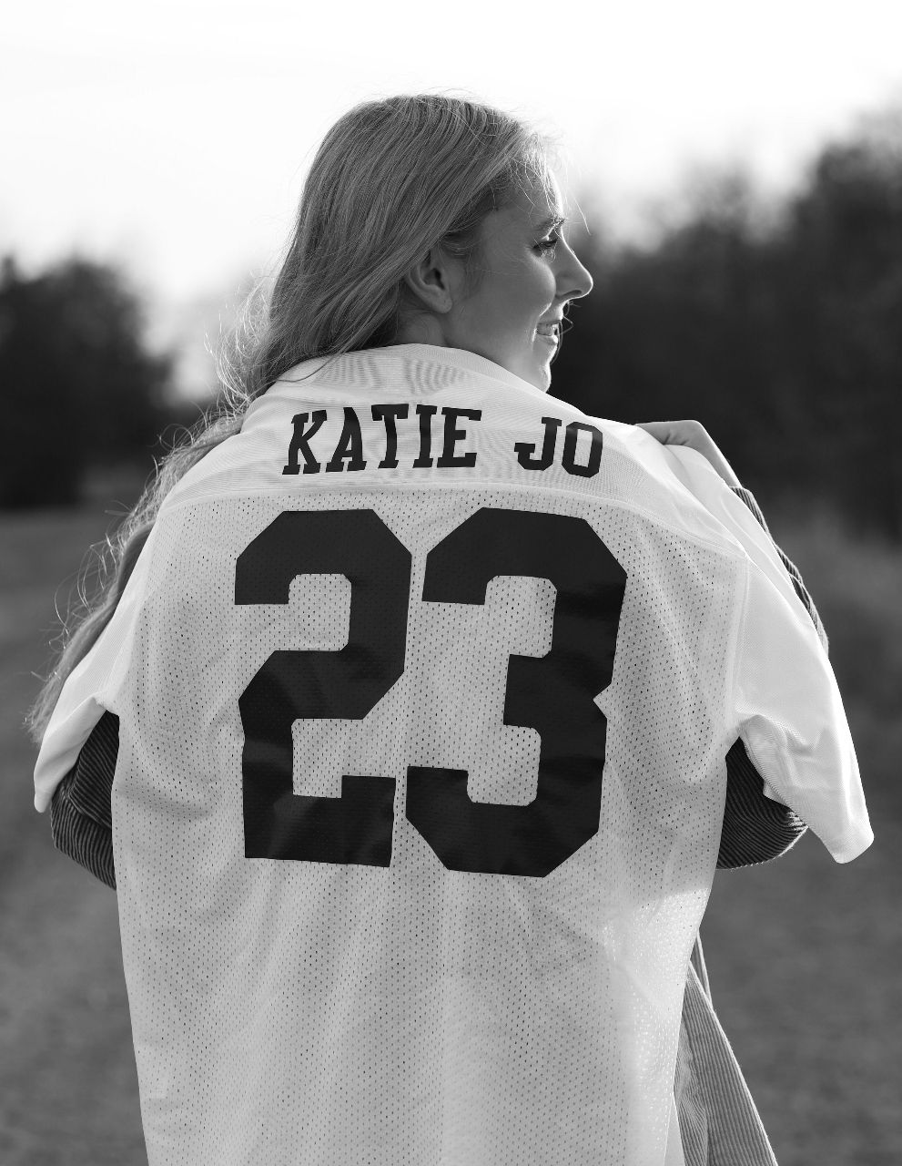 A black and white photo shows someone wearing a white jersey with number 23 and 'KATIE JO' text from behind.