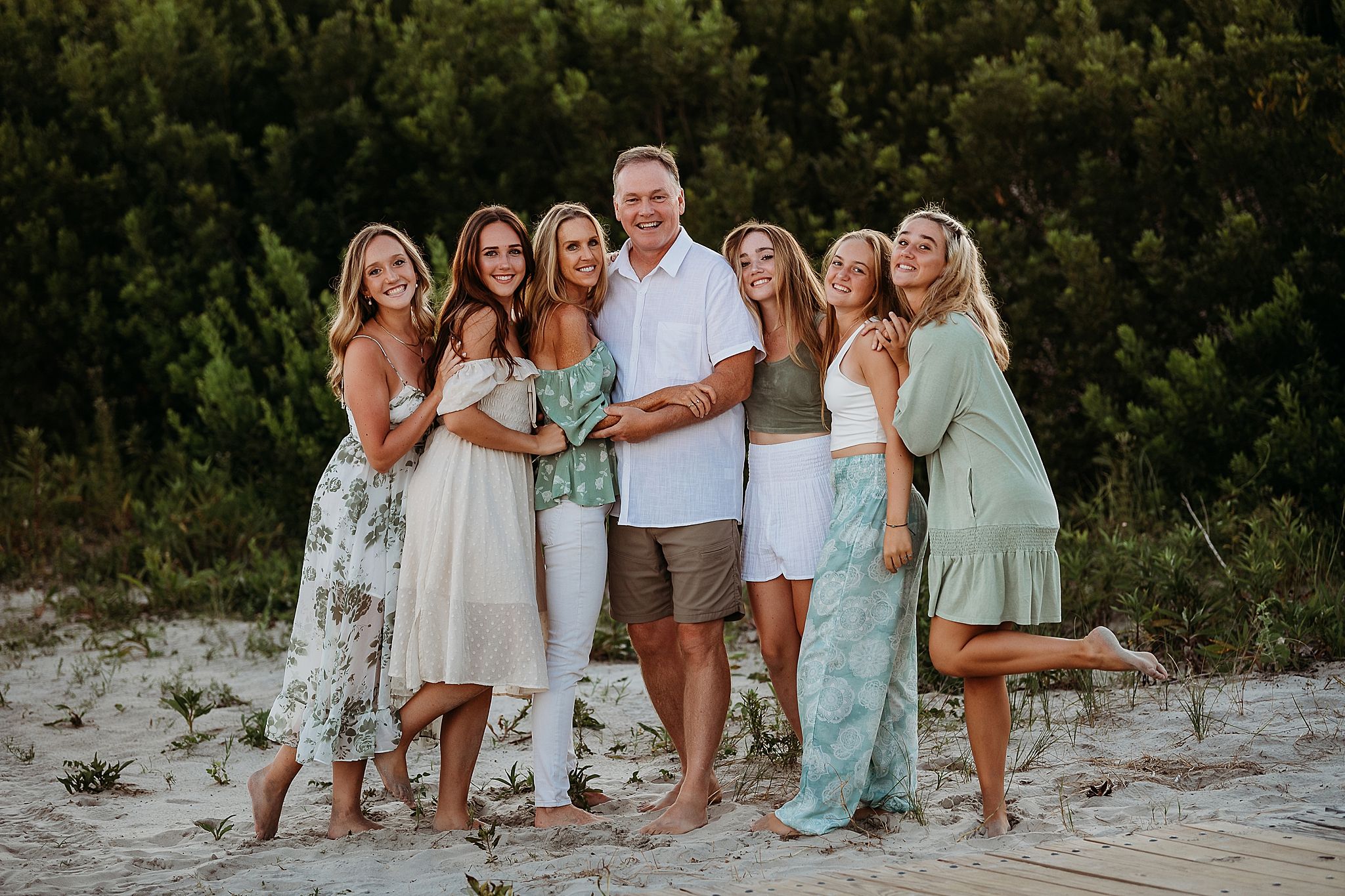 A family group wearing coordinated white and mint green outfits poses together on a sandy beach at sunset.
