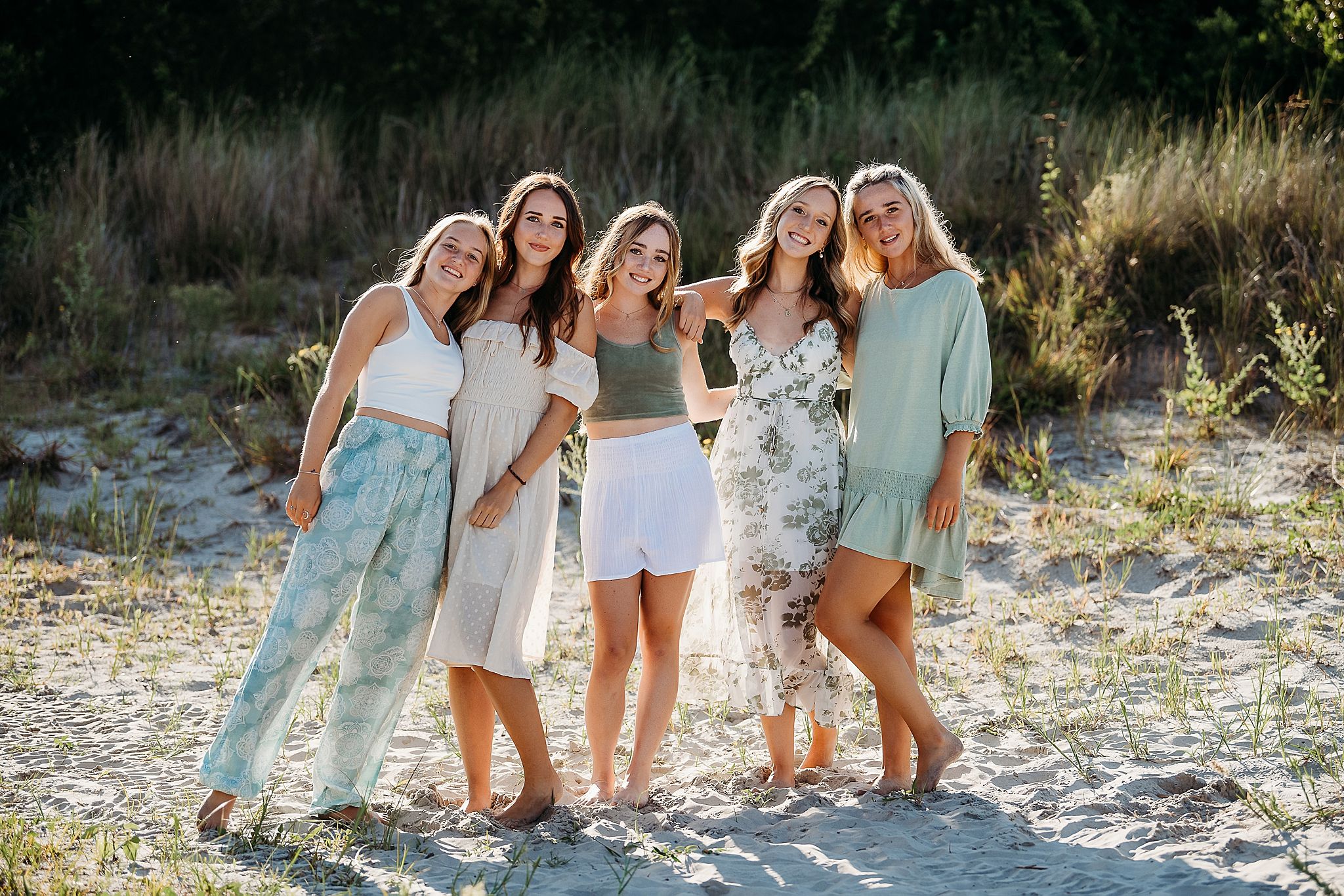 A group in pastel and white outfits walking and laughing together on the beach at sunset.