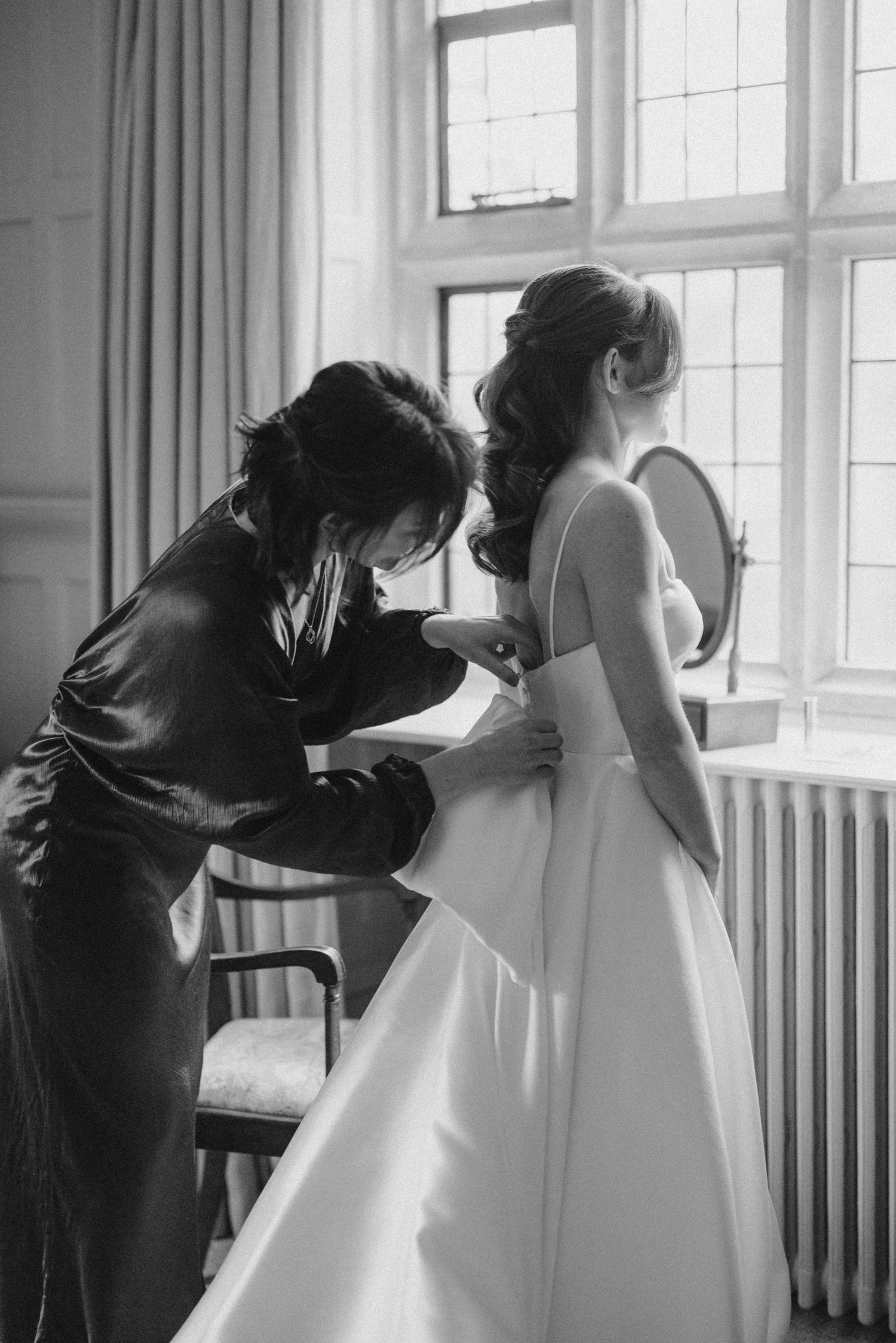 A sequence of black and white photos showing a seamstress helping adjust a white wedding dress during a fitting.