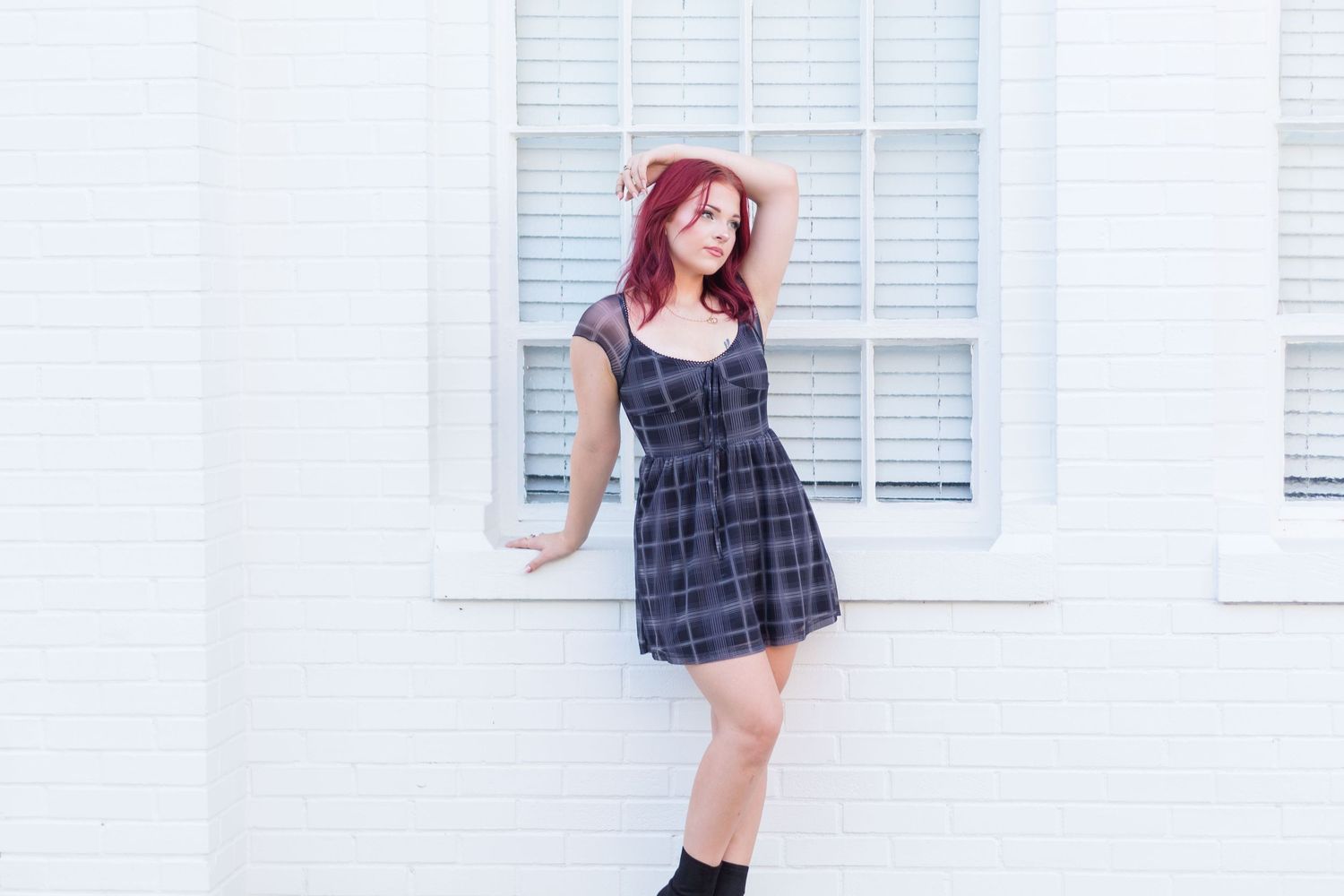 High school senior leaning on white wall in front of window.