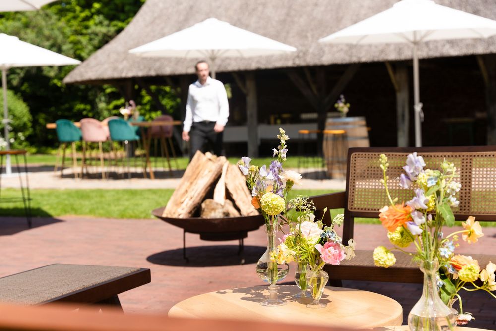 Outdoor patio area with white umbrellas, wooden furniture, and a fire pit surrounded by floral arrangements.