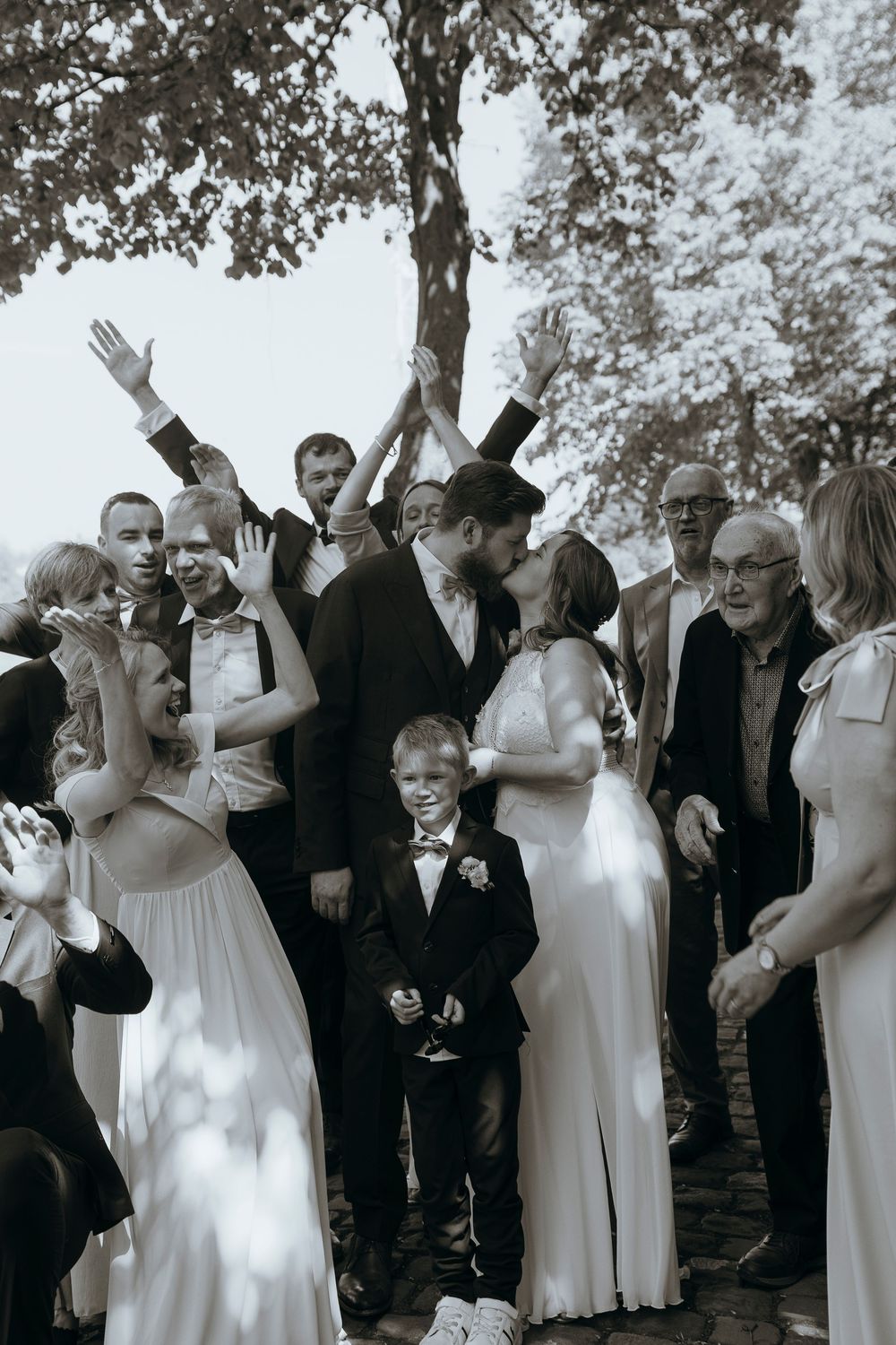 Joyous wedding celebration with guests laughing and cheering under a tree.