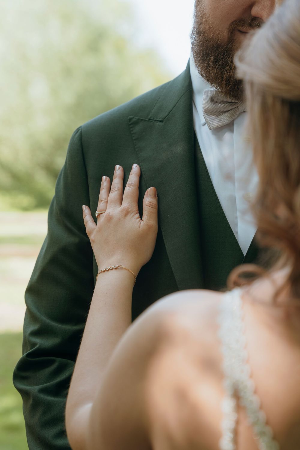 Close-up of hands touching a green suit jacket during an intimate wedding moment outdoors.