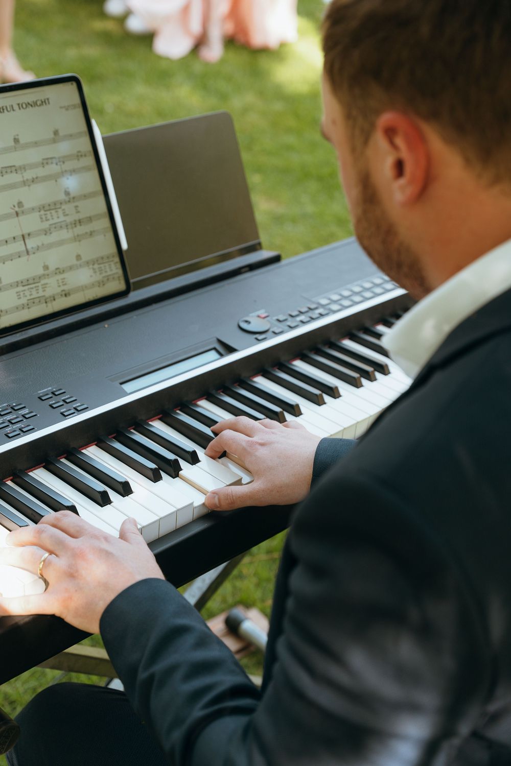 Musician playing a digital piano keyboard outdoors at a wedding event.