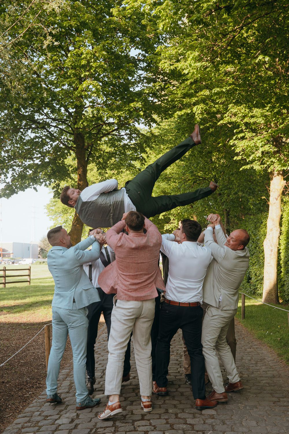 Groomsmen lift and support their friend horizontally in a fun outdoor photo.