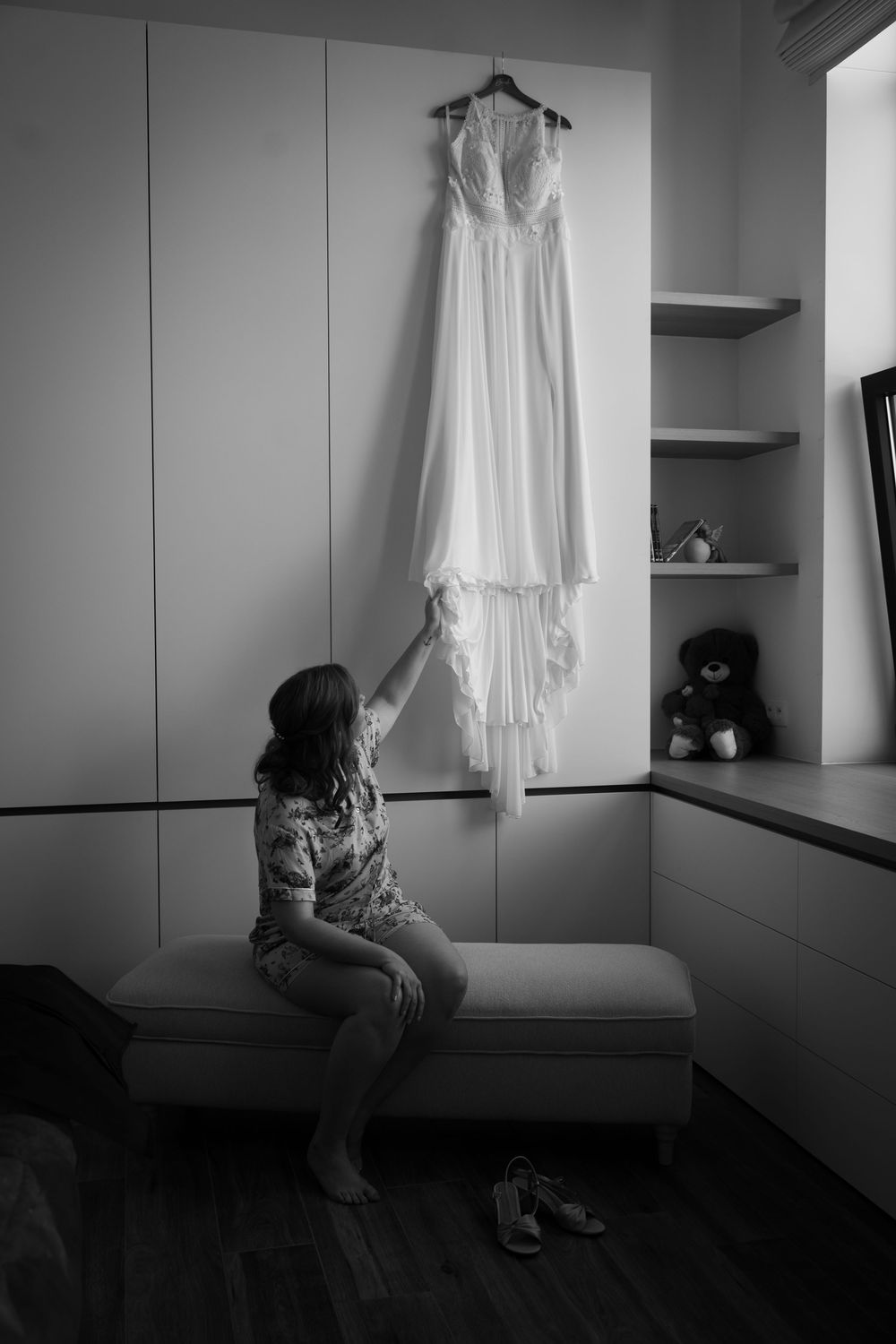 A white wedding dress hangs elegantly on display while someone reaches up to touch it.