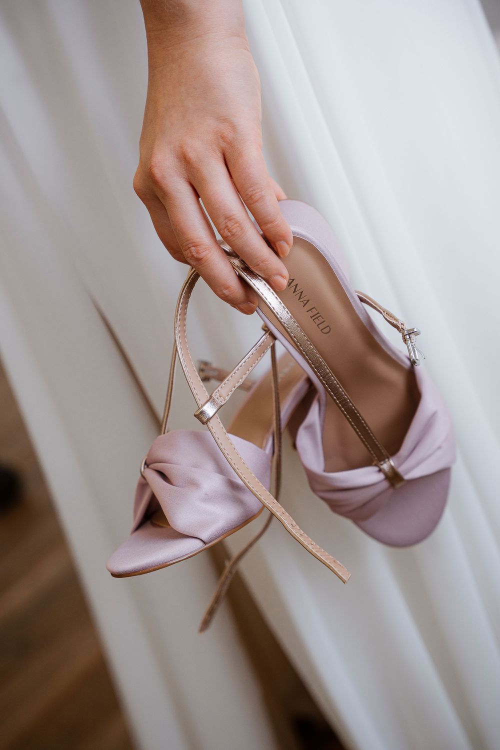 Delicate pink satin bridal shoes being held against a white fabric background.