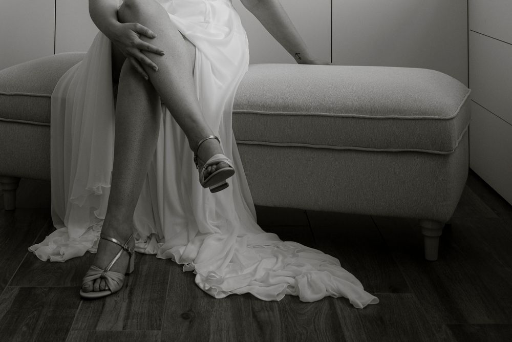 Black and white image showing the hem of a wedding dress against modern furniture.