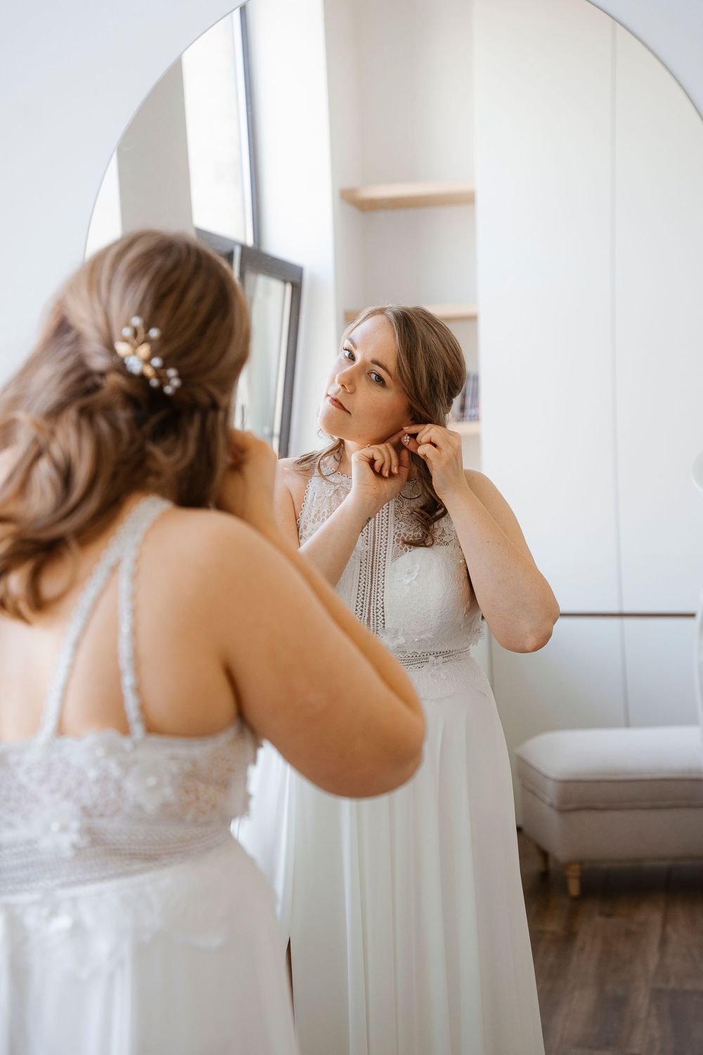 Close-up shots of a bride getting ready and putting on jewelry in front of a mirror in a white room.