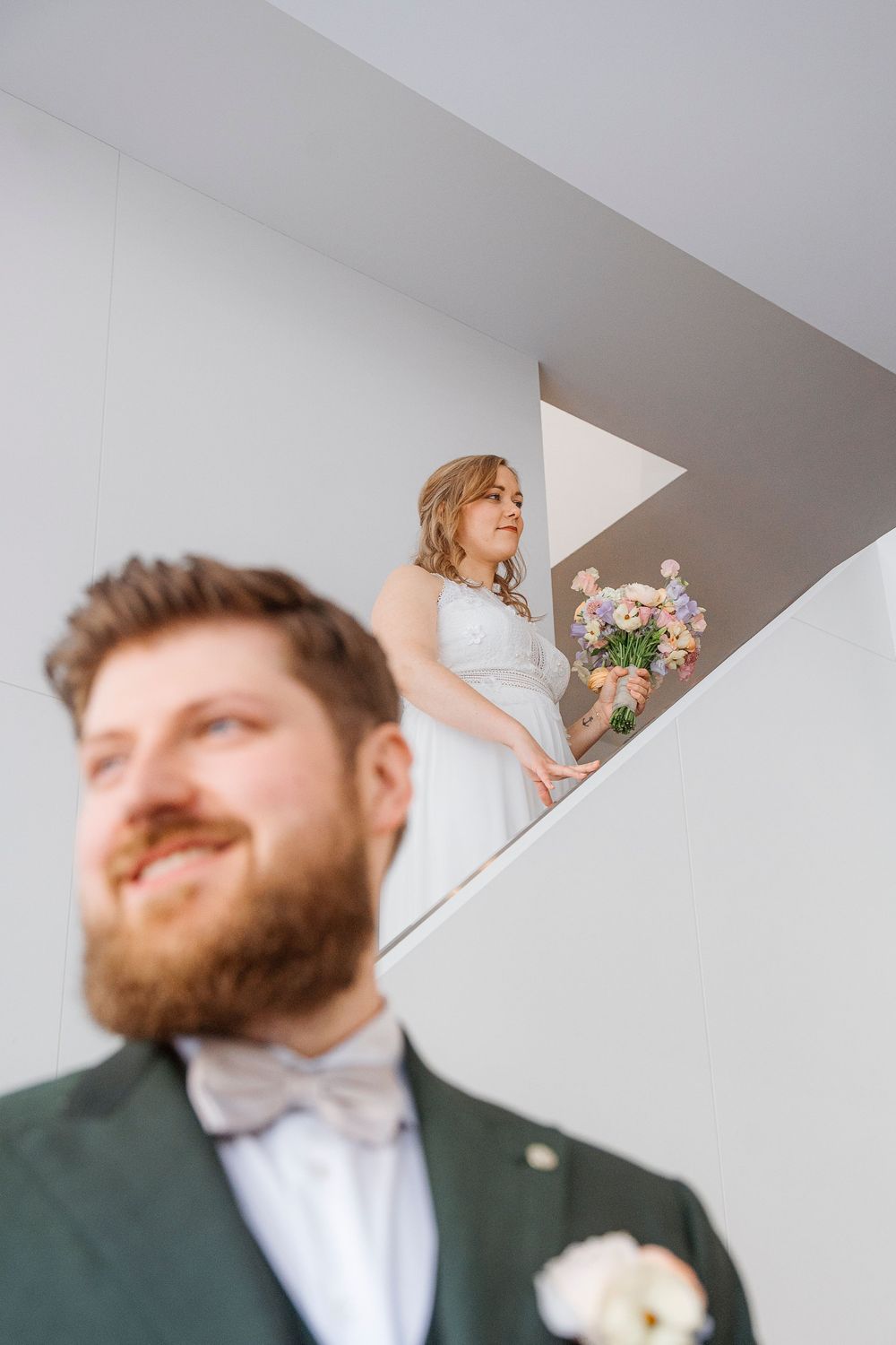 A couple shares a first-look wedding moment on a modern white staircase.