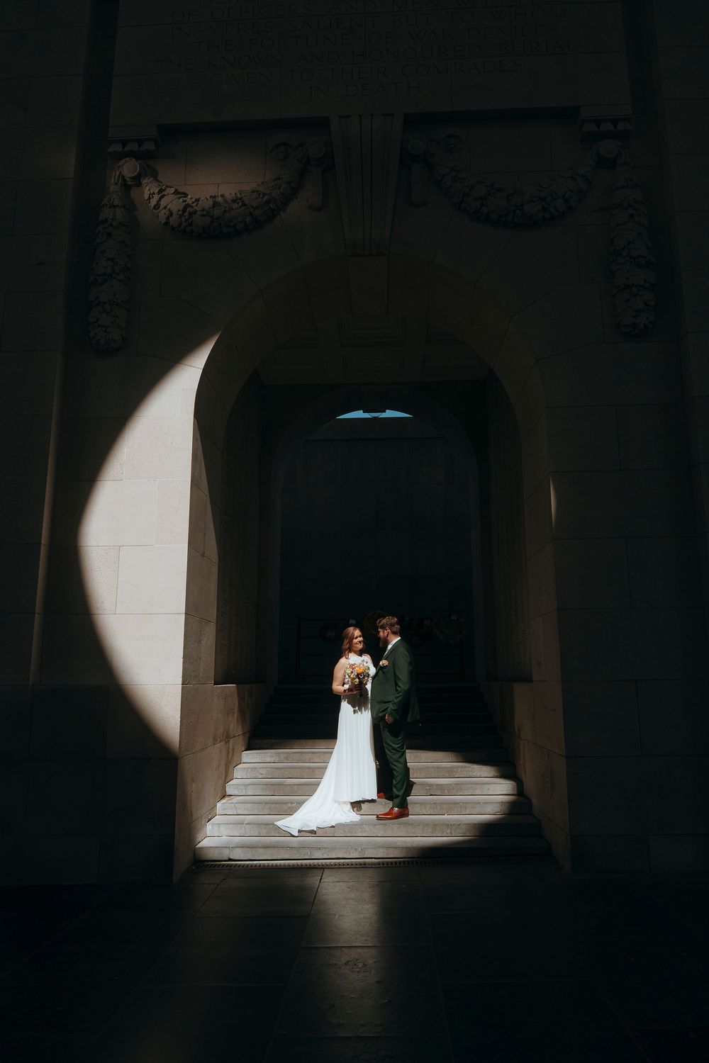 Dramatic spot lighting creates a moody wedding scene in a dark columned corridor.