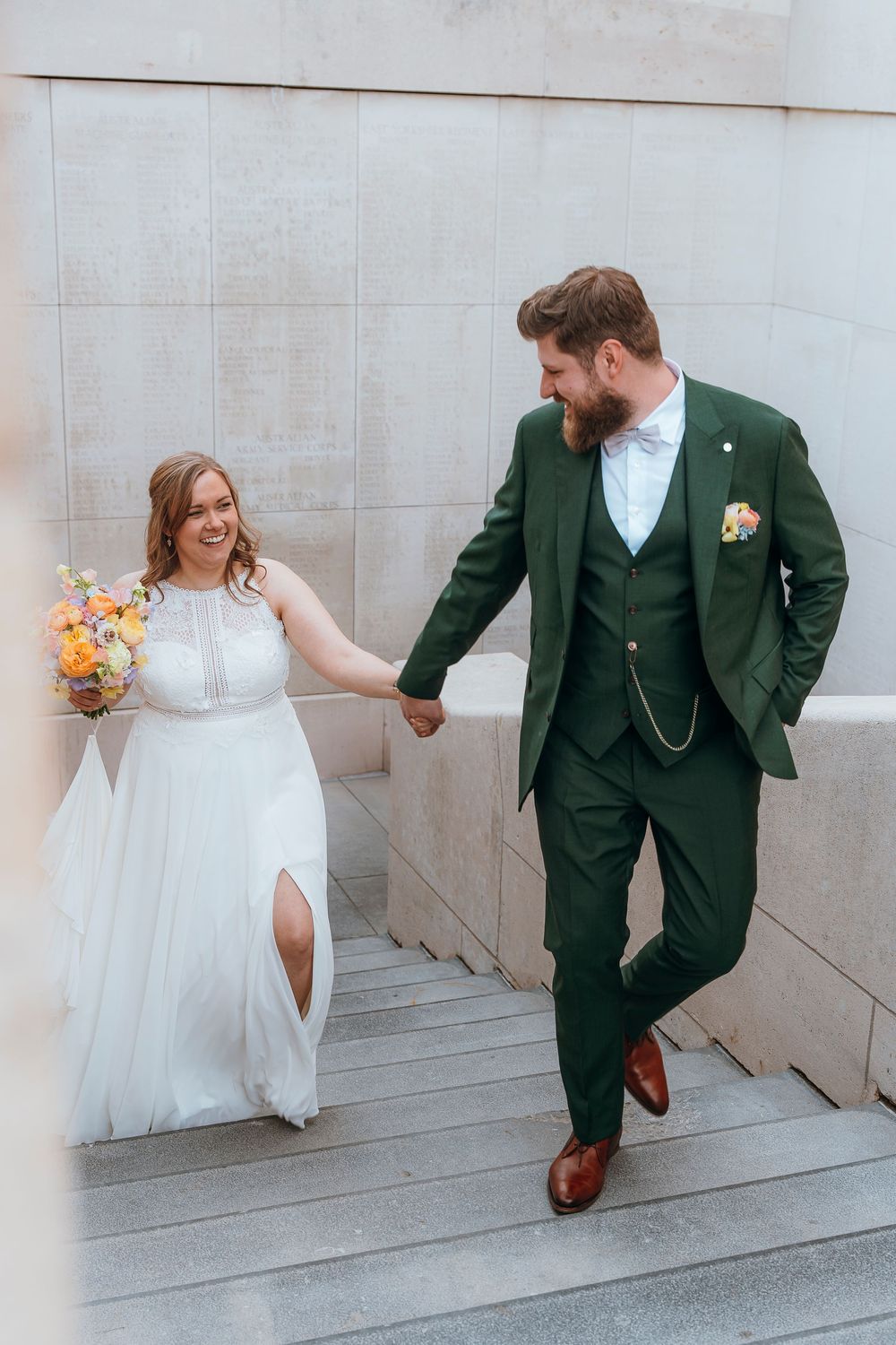 A couple in wedding attire descending marble stairs, with the groom wearing a distinctive green suit.