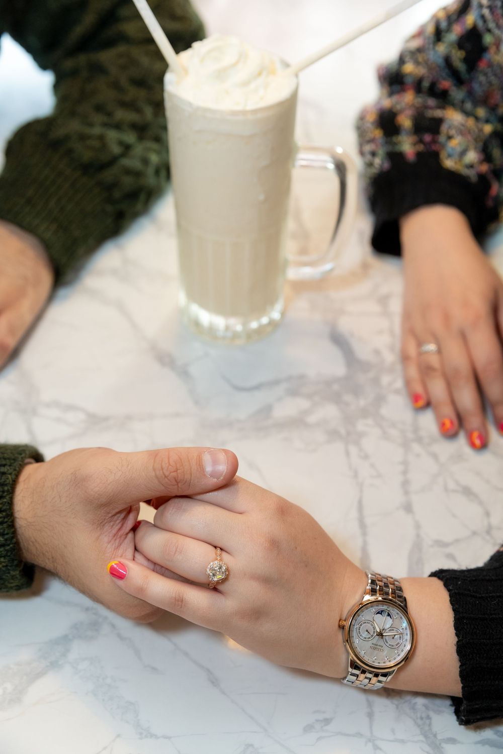 Closeup of couple holding hands with engagement ring in foregroumd and milkshake in background at Bel-Aire Diner in Astoria, Queens.
