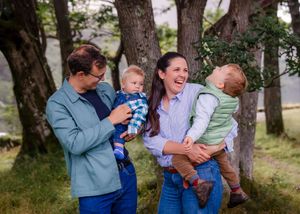 Parents with young children under trees smiling family photoshoot in the woods, candid moments.