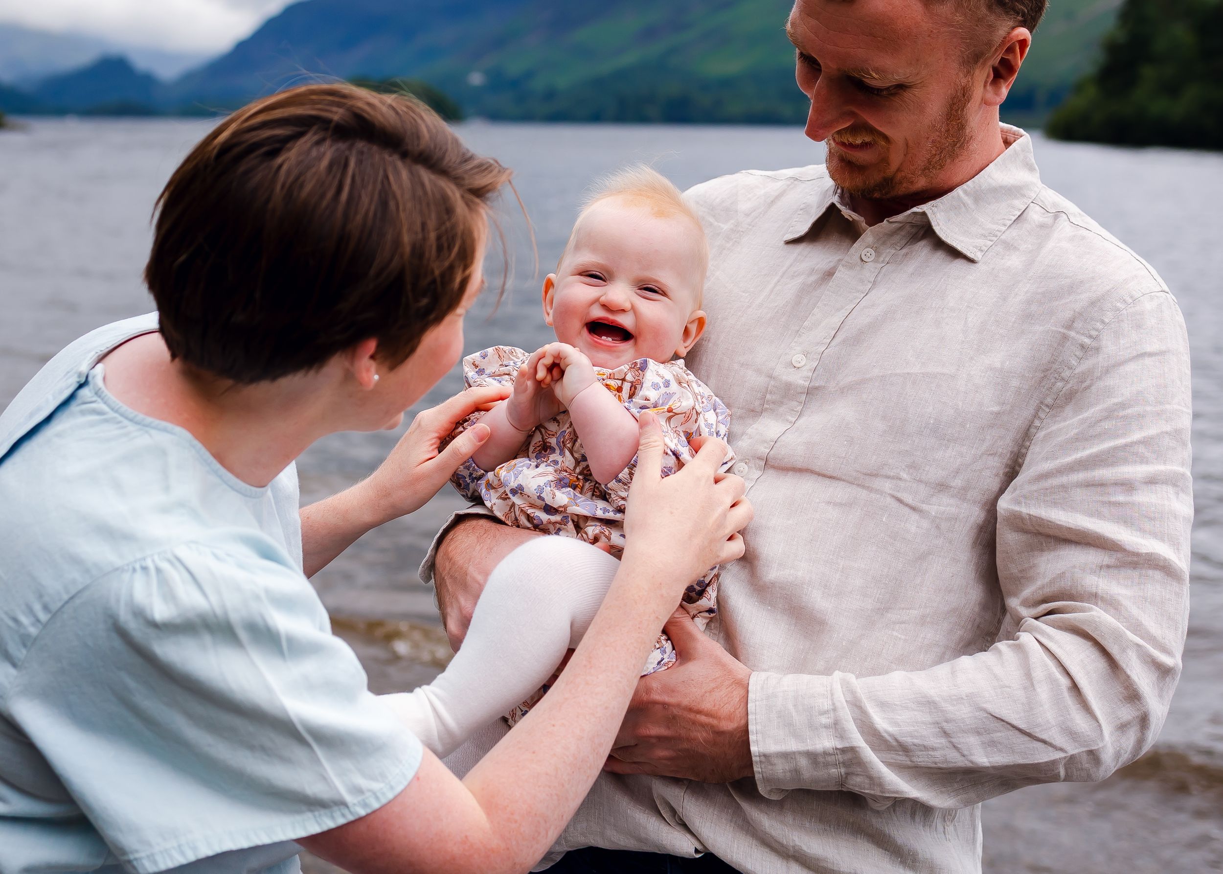 Parents smiling and playing with their baby outdoors family photographer near you.