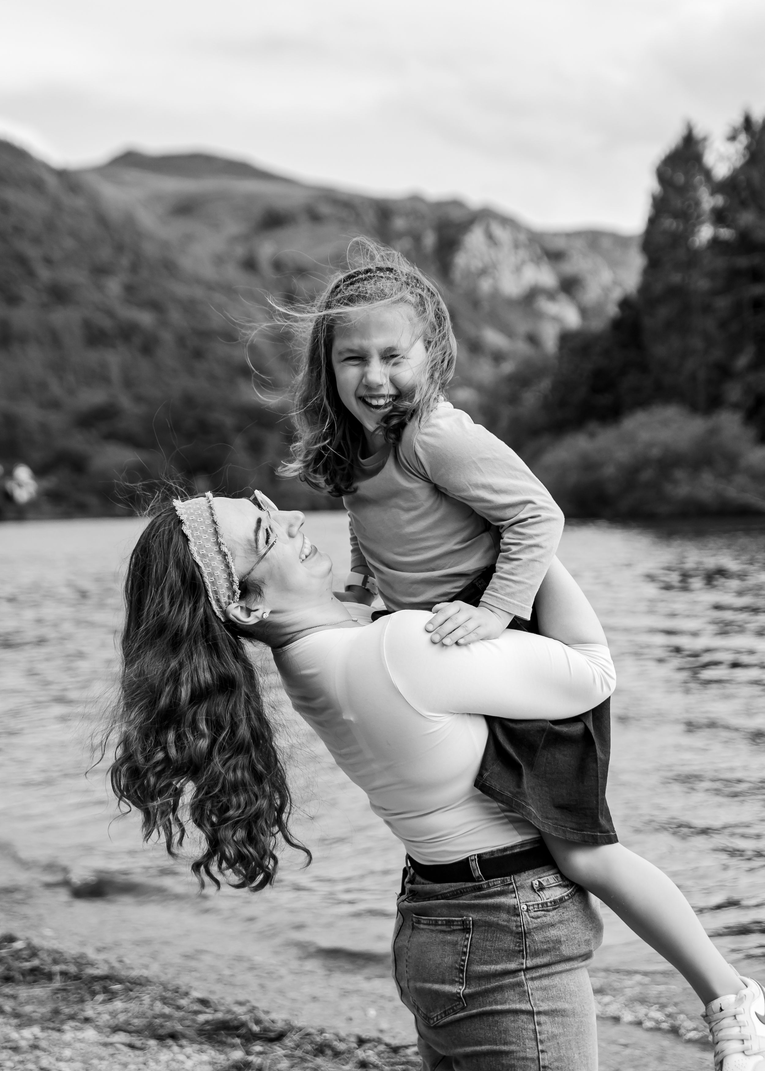 A mother lifts and spins her daughter by a lake. Family photography, candid lake photoshoot