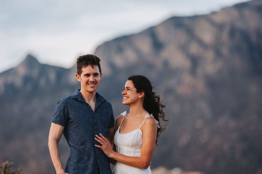 A romantic couple shares a joyful moment together against a backdrop of rugged mountain peaks.