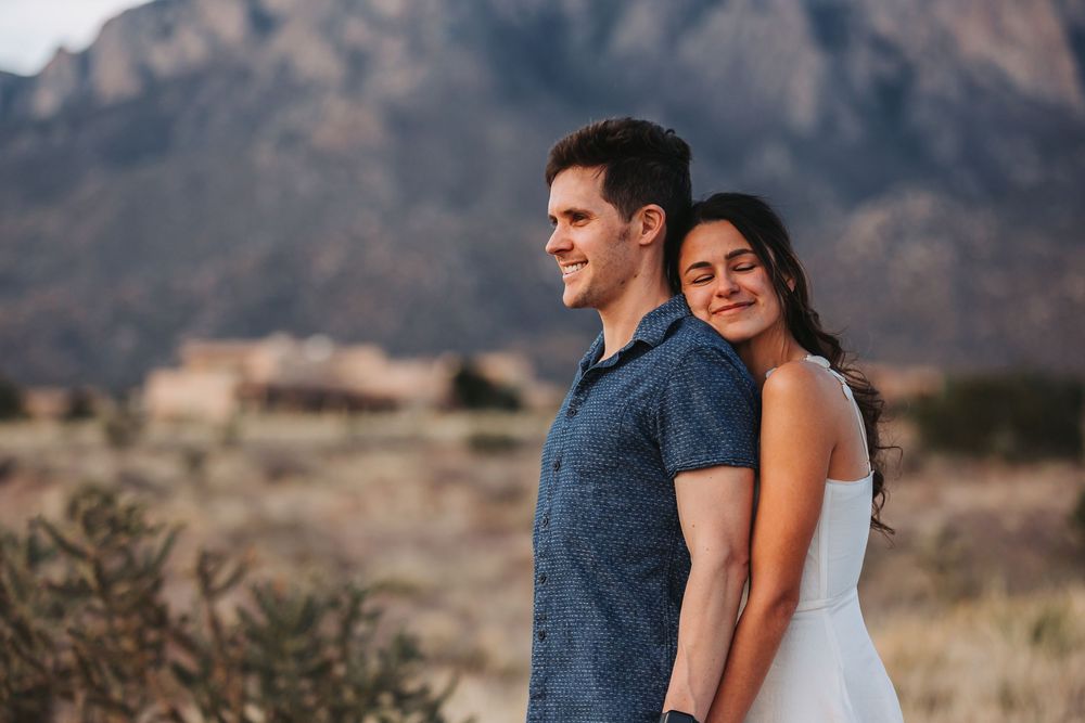 A couple embraces while enjoying the scenic desert landscape with mountains in the distance.