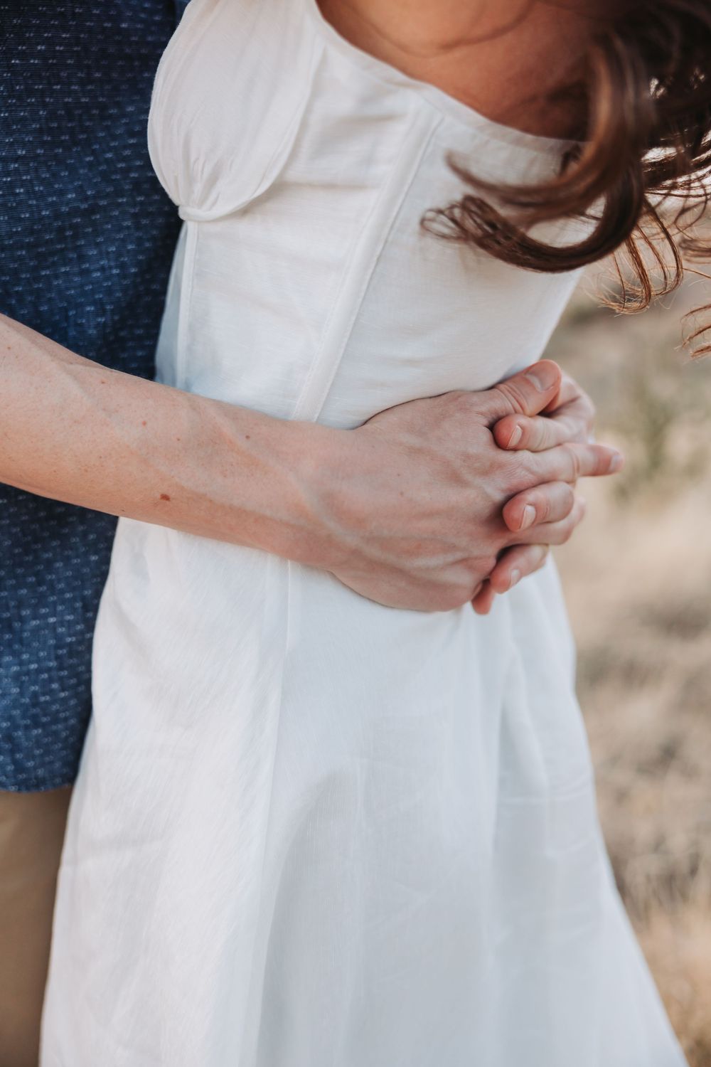 Close-up detail view of hands gently resting on a white flowy dress by denim textured backdrop.