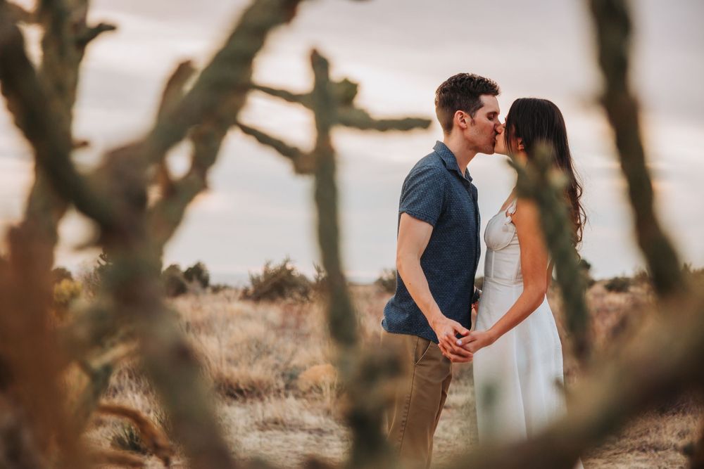 A romantic desert photoshoot with two people holding hands among desert plants at sunset.