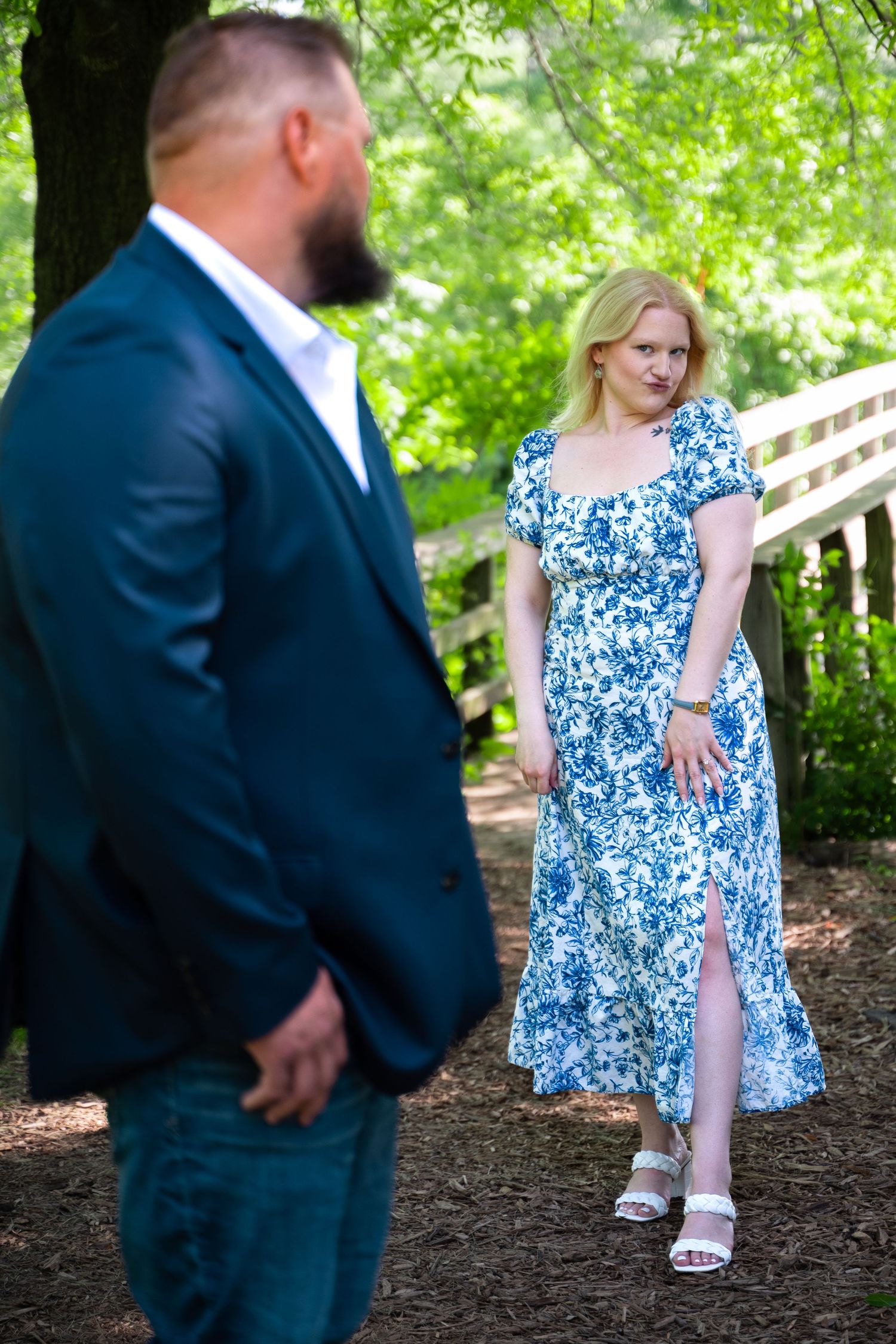 Bride-to-be in white and blue floral dress makes kissy face at fiancé standing with back to camera at Powell Gardens