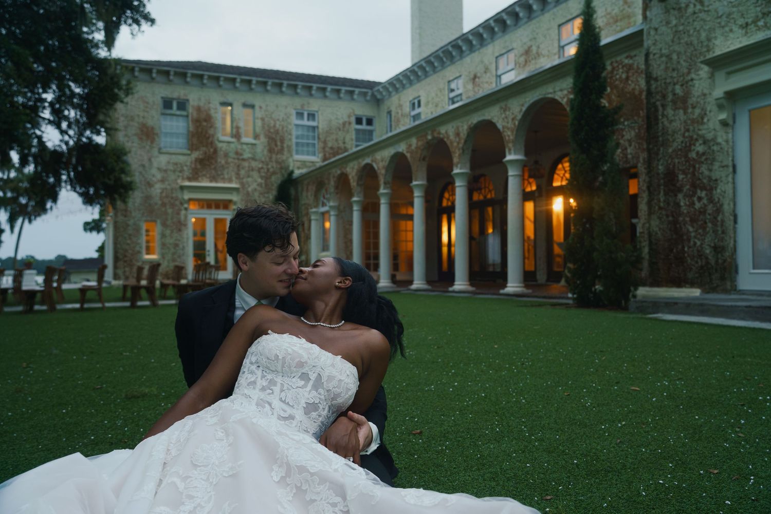 Close-up of hands wearing wedding rings, with bride in lace sleeve and groom in black suit exchanging a tender touch.